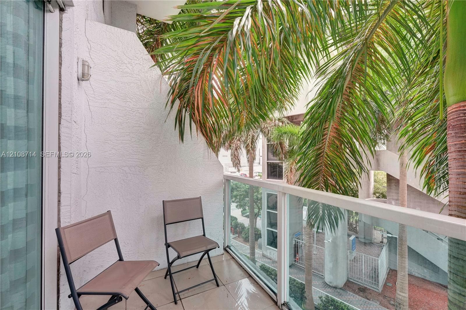 Private balcony featuring textured stucco walls, large-format tile flooring, and a glass-paneled railing