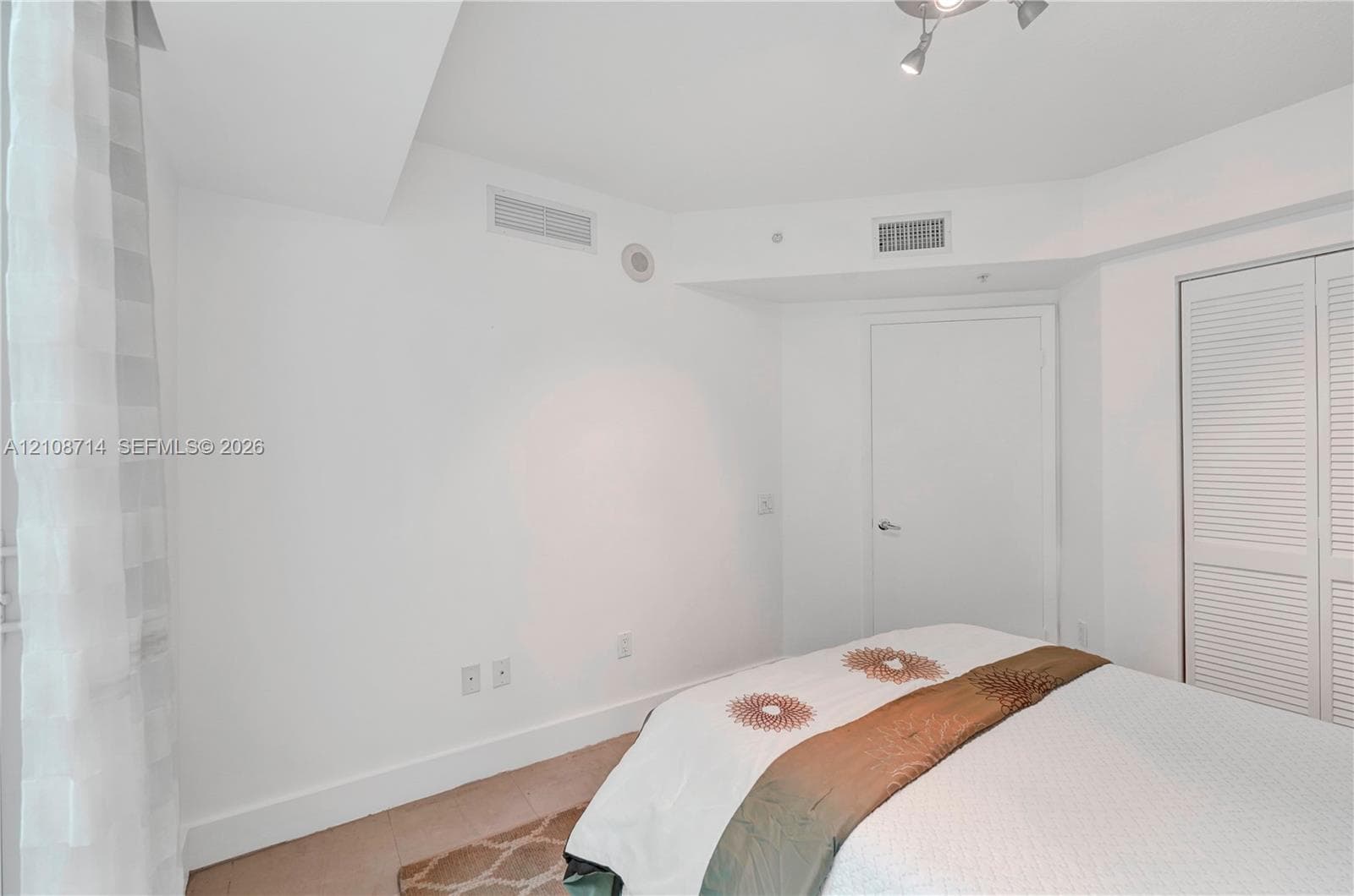Neutral interior room featuring white walls, white louvered closet doors, and a ceiling-mounted adjustable track light fixture