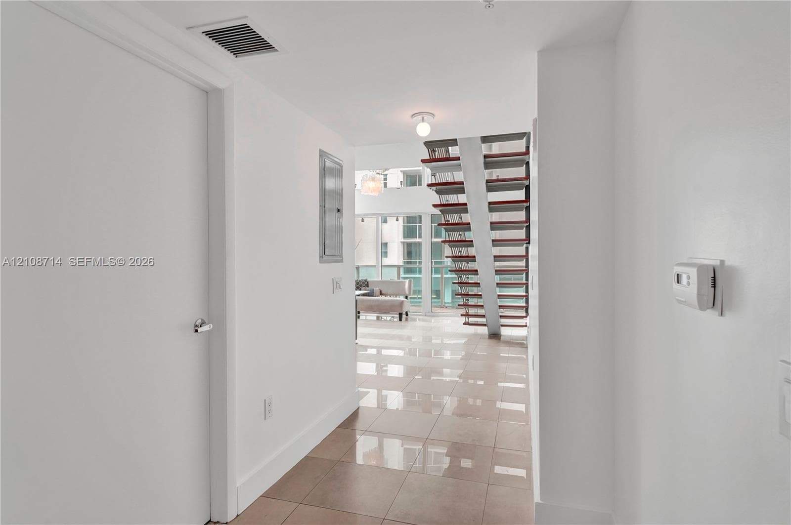 Open-concept interior featuring large-format tile flooring, a custom staircase with metal supports and open risers, and full-height glass windows