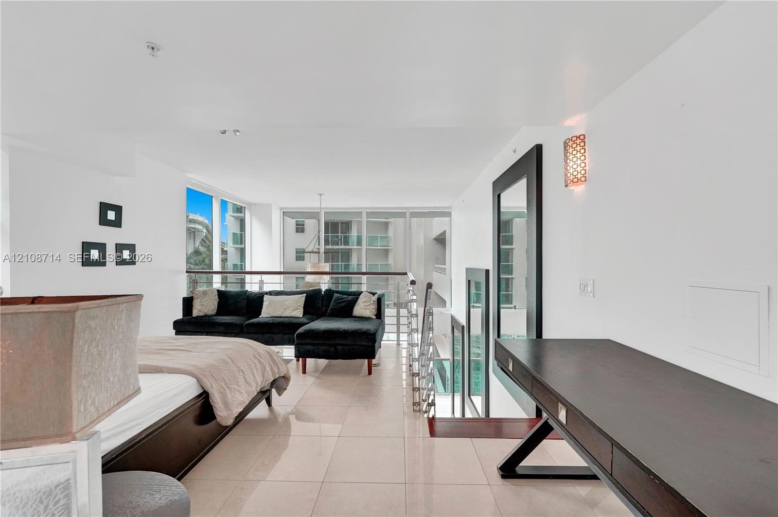 Open-concept loft area featuring large-format tile flooring, a built-in dark wood desk, floor-to-ceiling windows, and a metal-railing staircase