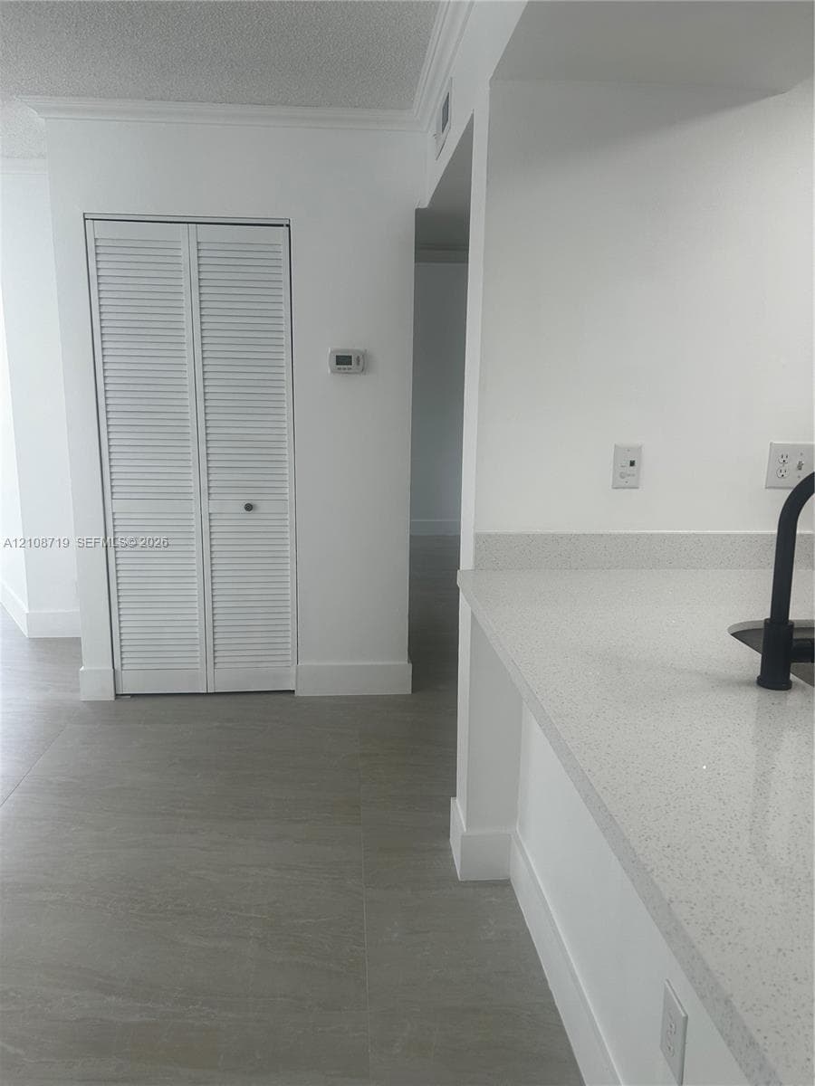 Neutral-toned tile flooring, quartz countertops, matte black faucet, and white louvered-door closet