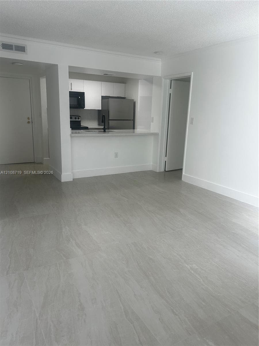 Open-concept living space featuring large-format tile flooring, white cabinetry, a breakfast bar, and stainless steel appliances