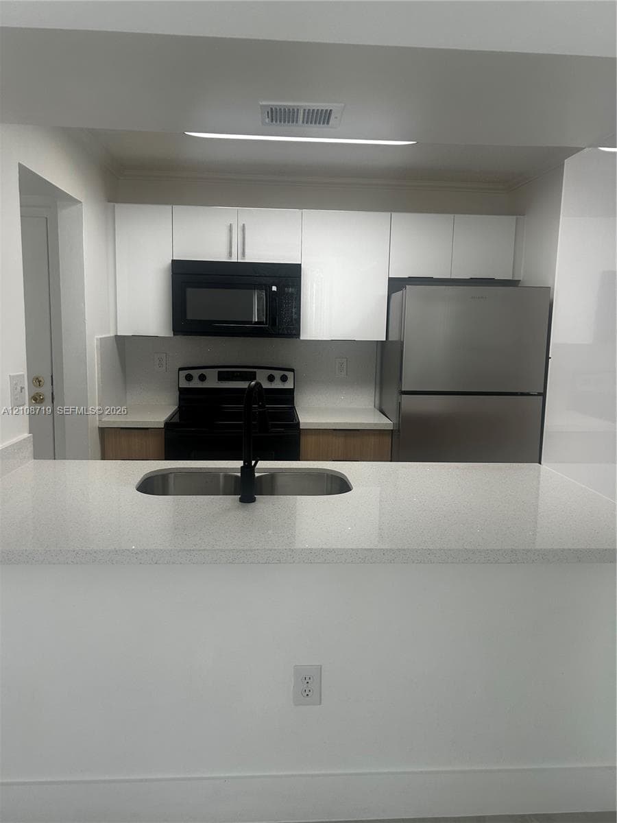 Kitchen featuring white flat-panel cabinetry, quartz countertops, stainless steel appliances, and a dual-basin undermount sink with a matte black faucet