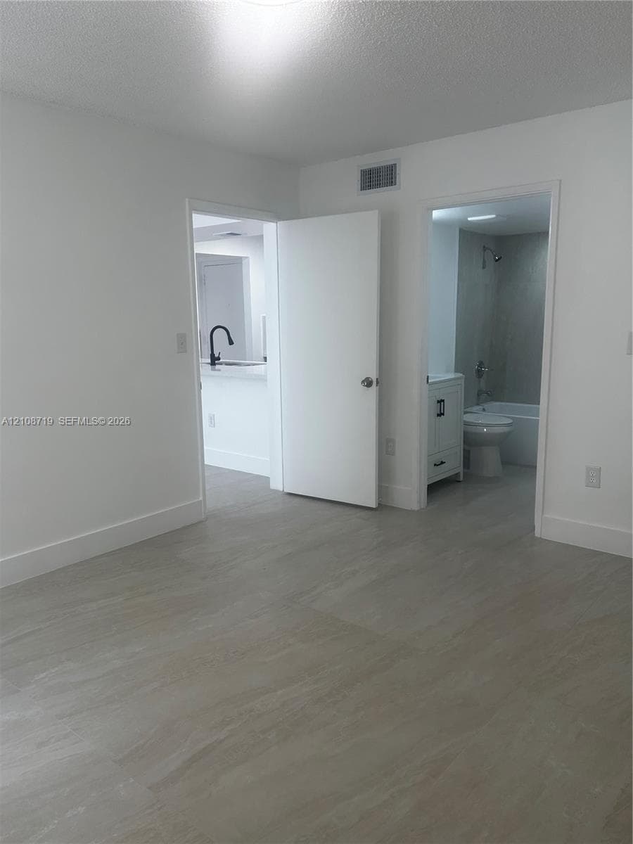 Neutral-toned tile flooring, white-painted interior doors, a bathroom featuring a vanity with shaker-style cabinetry, and a kitchen area highlighting a high-arc matte black faucet