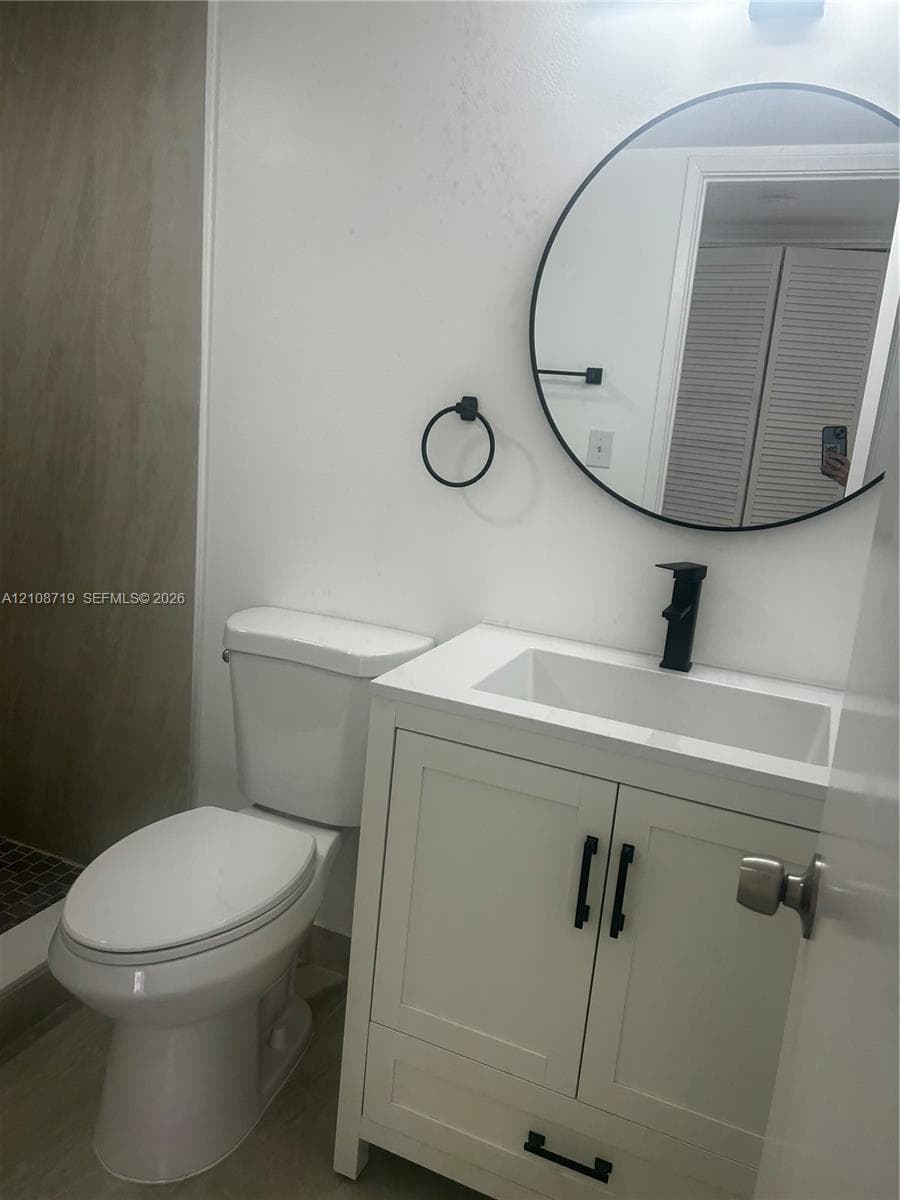 White vanity cabinet featuring a rectangular basin, matte black faucet, and matching cabinet hardware, accented by a circular wall mirror and circular towel ring