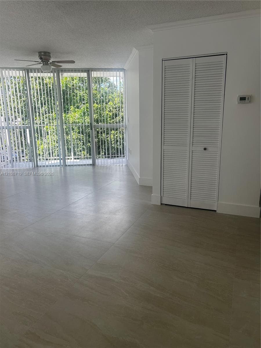 Large-format tile flooring, ceiling fan with integrated light, floor-to-ceiling glass panel windows, and white louvered closet doors