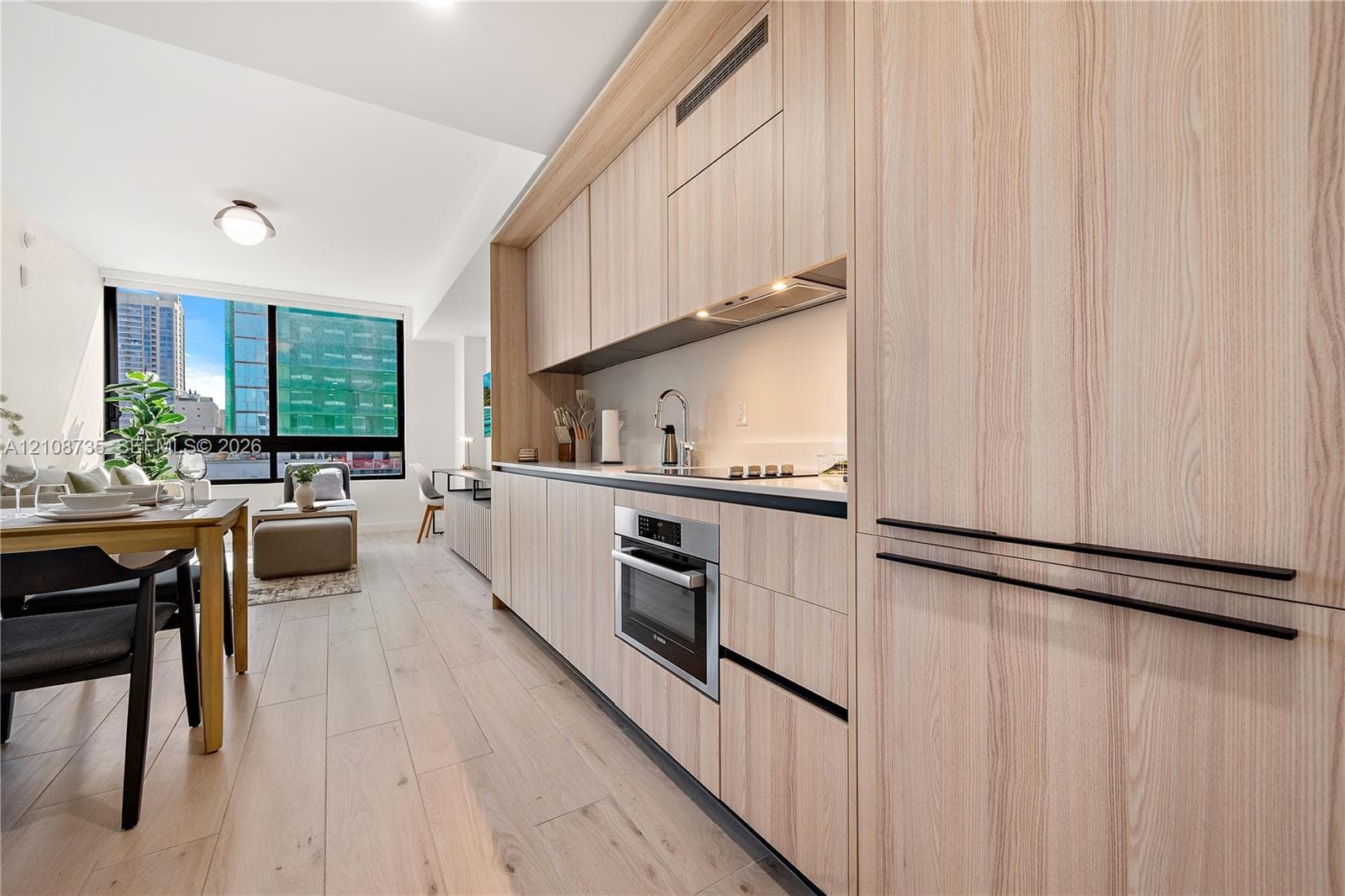 Kitchen featuring wood-finish cabinetry with matte black pulls, integrated stainless steel appliances, a light-toned countertop, and wood-finish flooring throughout