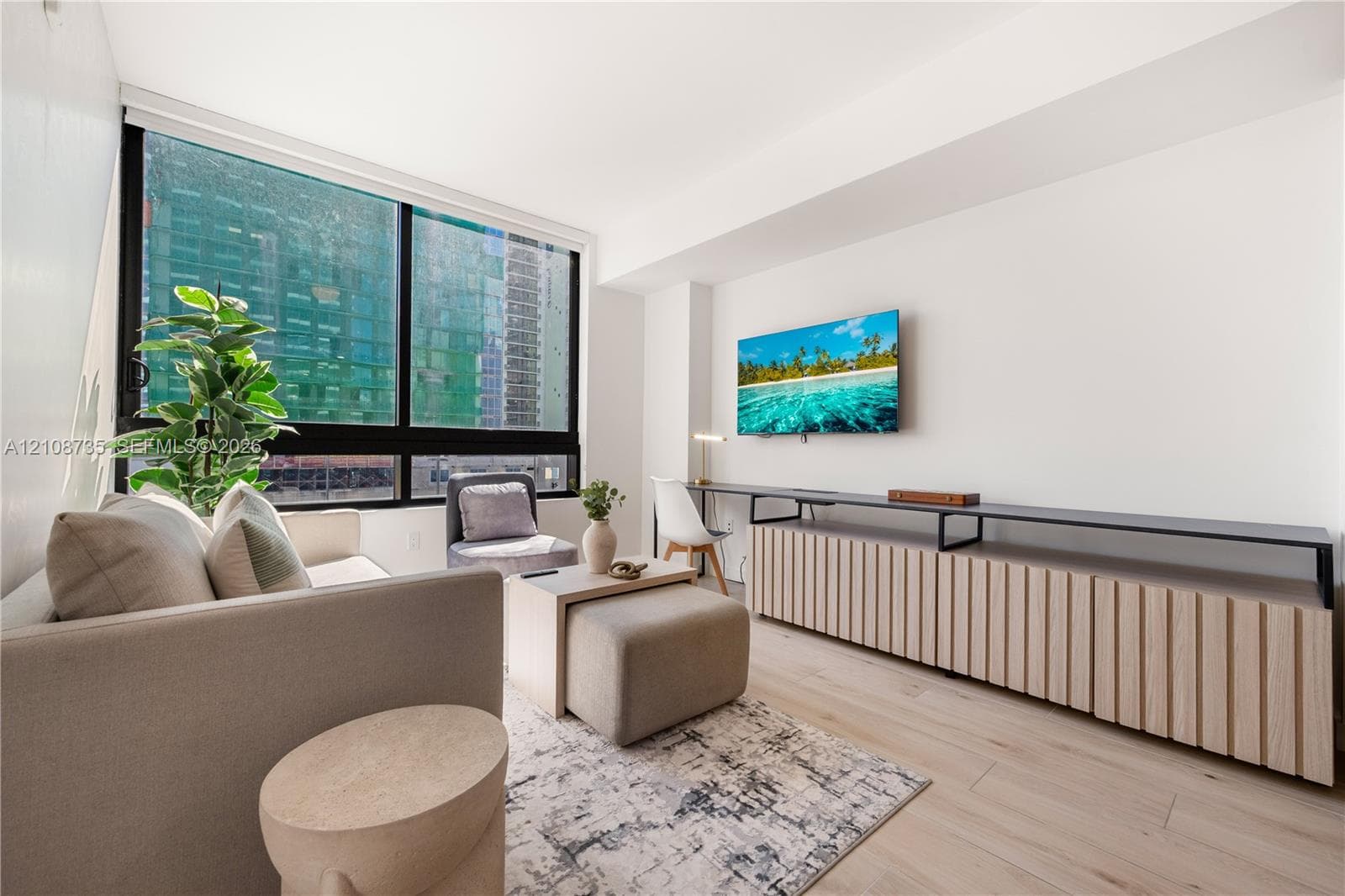 Floor-to-ceiling windows, wood-finish flooring, and built-in fluted cabinetry with a metal-frame desktop surface