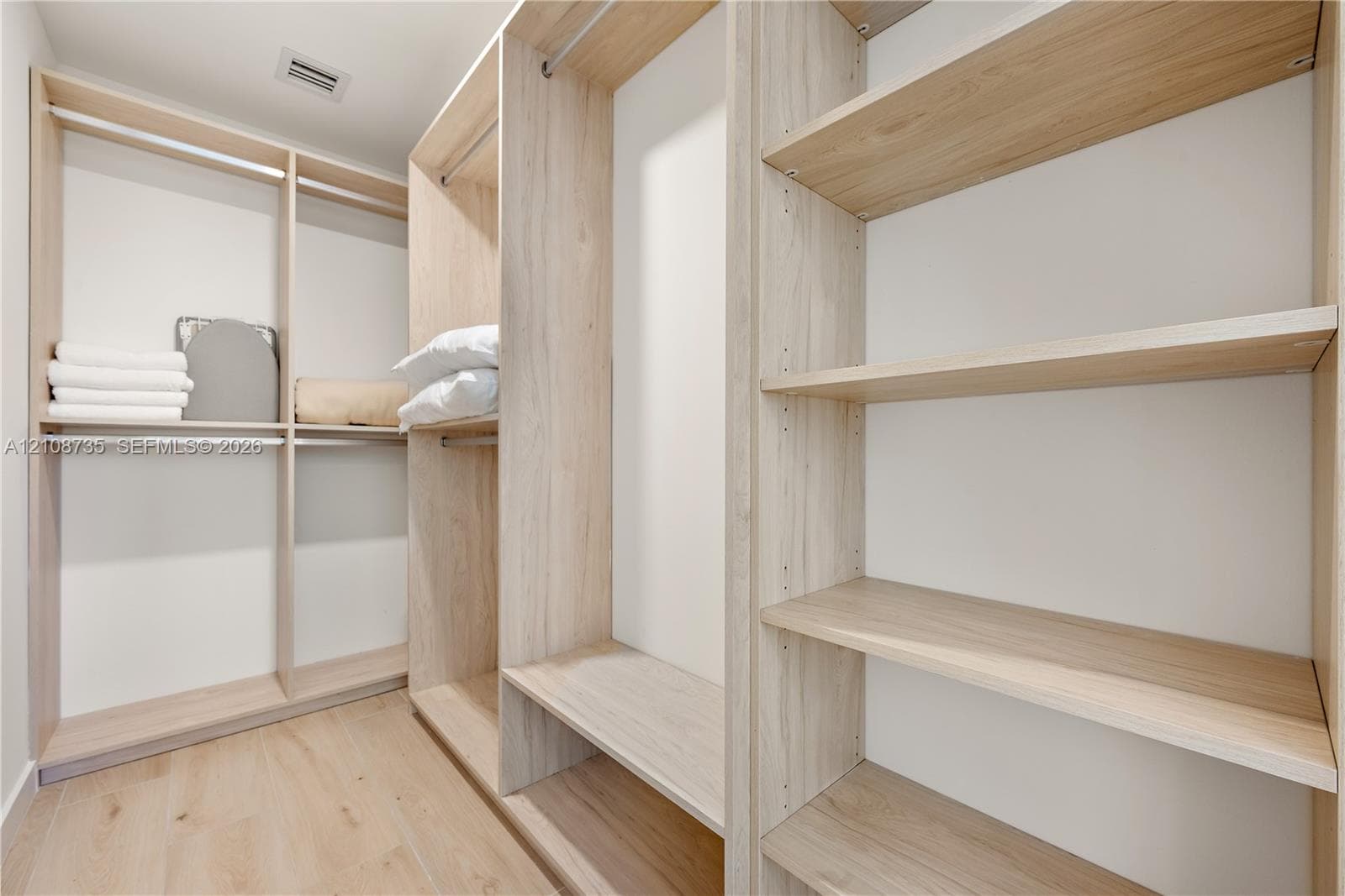Walk-in closet featuring custom wood-finish shelving, integrated hanging rods, and wood-finish flooring