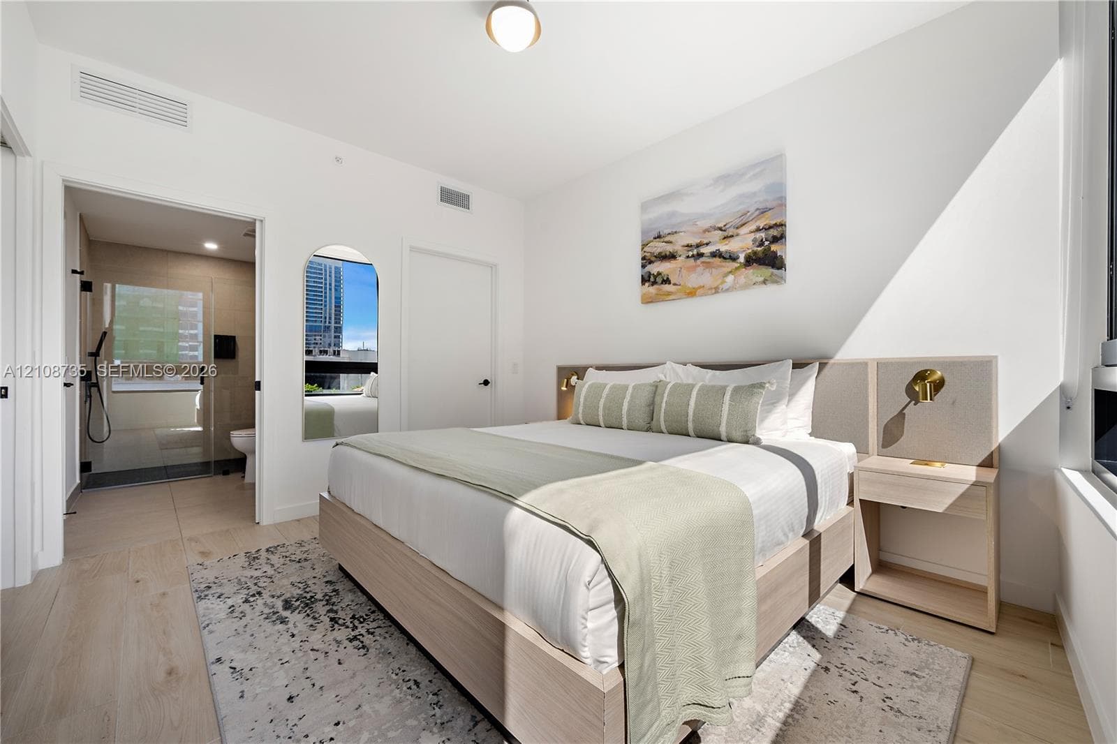 Bedroom featuring light wood-finish flooring, a built-in headboard with integrated lighting, and an arched wall mirror