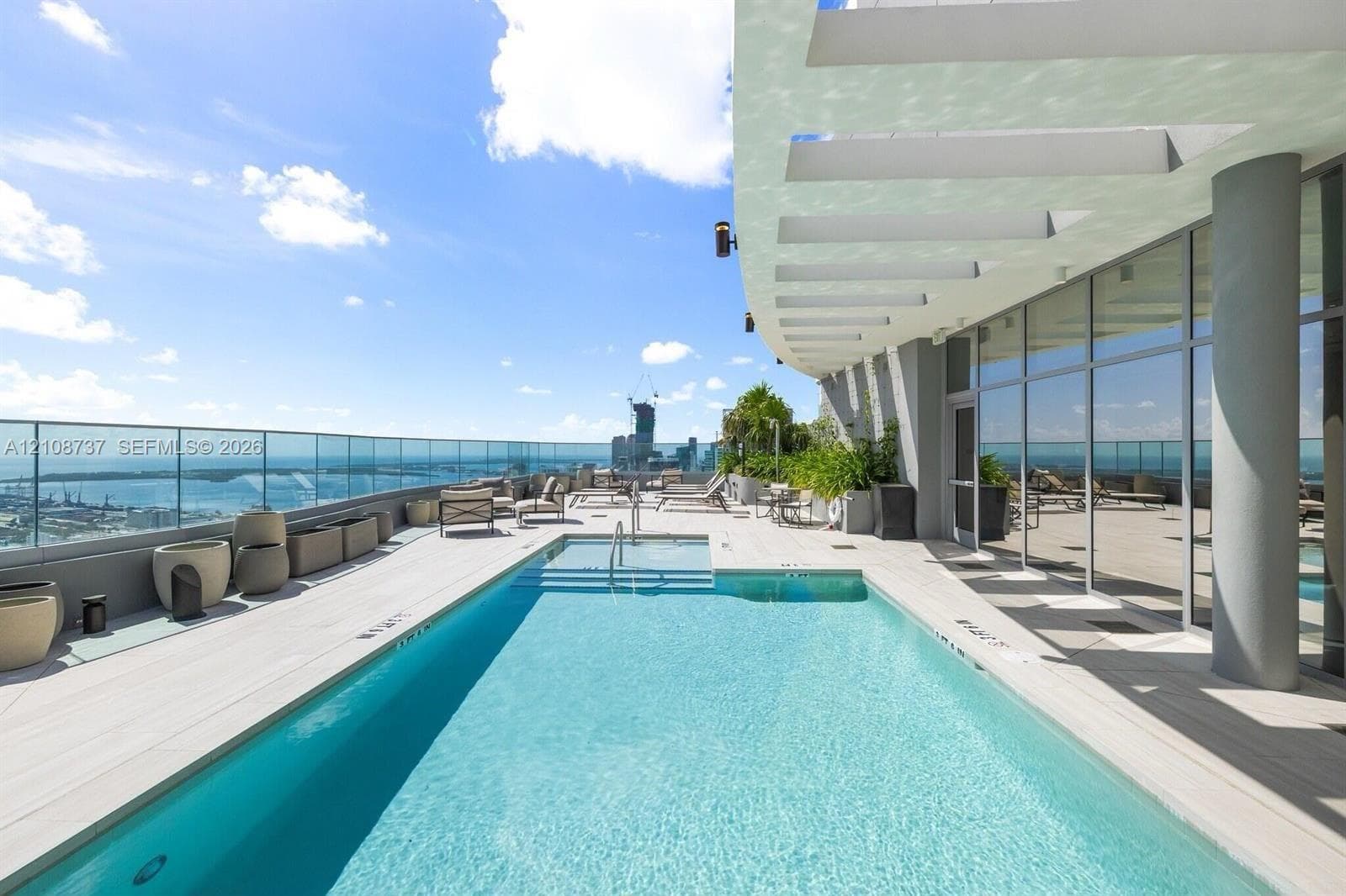 Rooftop terrace featuring an infinity-edge swimming pool, glass perimeter railing, wood-finish decking, and floor-to-ceiling window walls