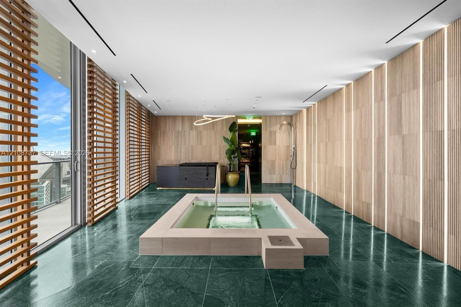 Sunken spa with a stone surround, floor-to-ceiling wood-paneled walls with integrated vertical lighting, green stone flooring, and expansive wood-slat privacy screens
