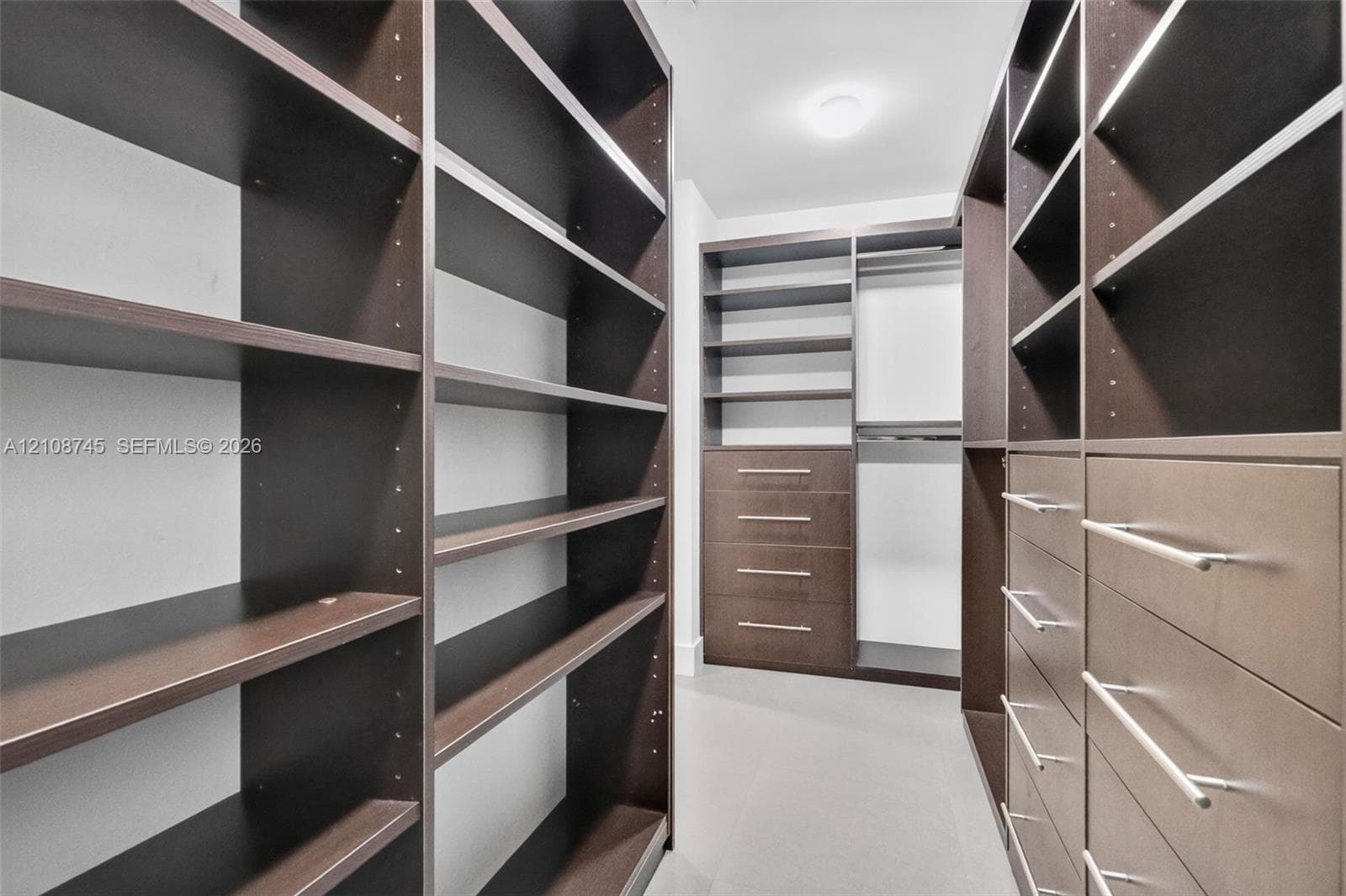 Walk-in closet featuring extensive custom dark-wood cabinetry, adjustable shelving, integrated drawer banks with horizontal hardware, and hanging rods