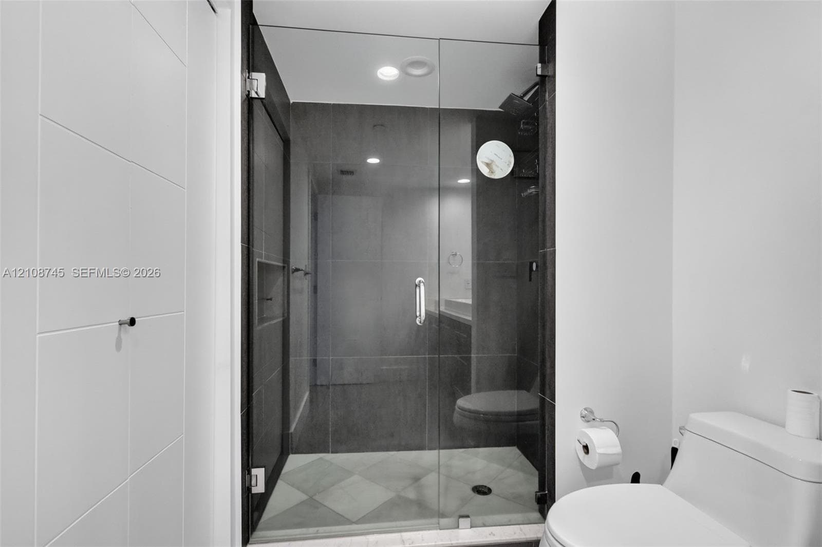 Walk-in shower featuring a frameless glass door, dark wall tile, built-in recessed shelving, a rainfall showerhead, and a diamond-patterned floor tile