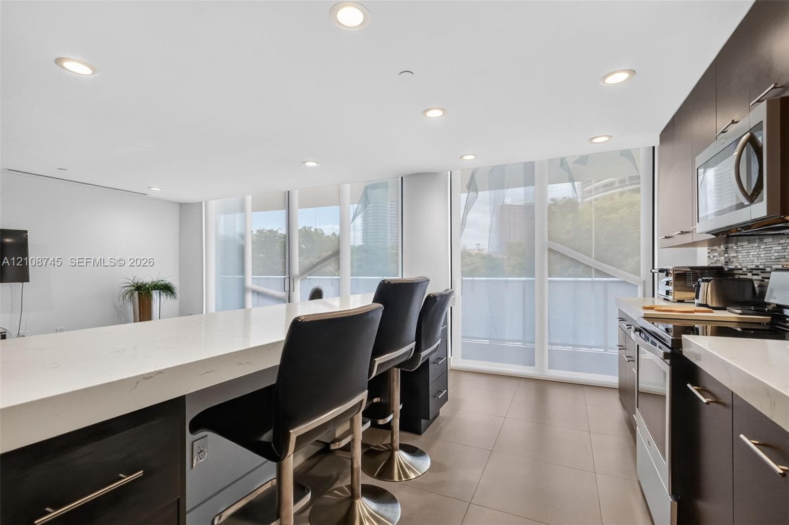 Kitchen featuring dark cabinetry, quartz countertops, tile flooring, recessed lighting, and floor-to-ceiling windows