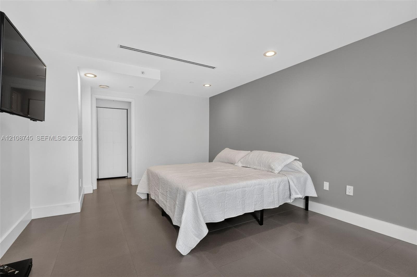 Interior space featuring large-format neutral floor tiling, a grey accent wall, and recessed ceiling lighting