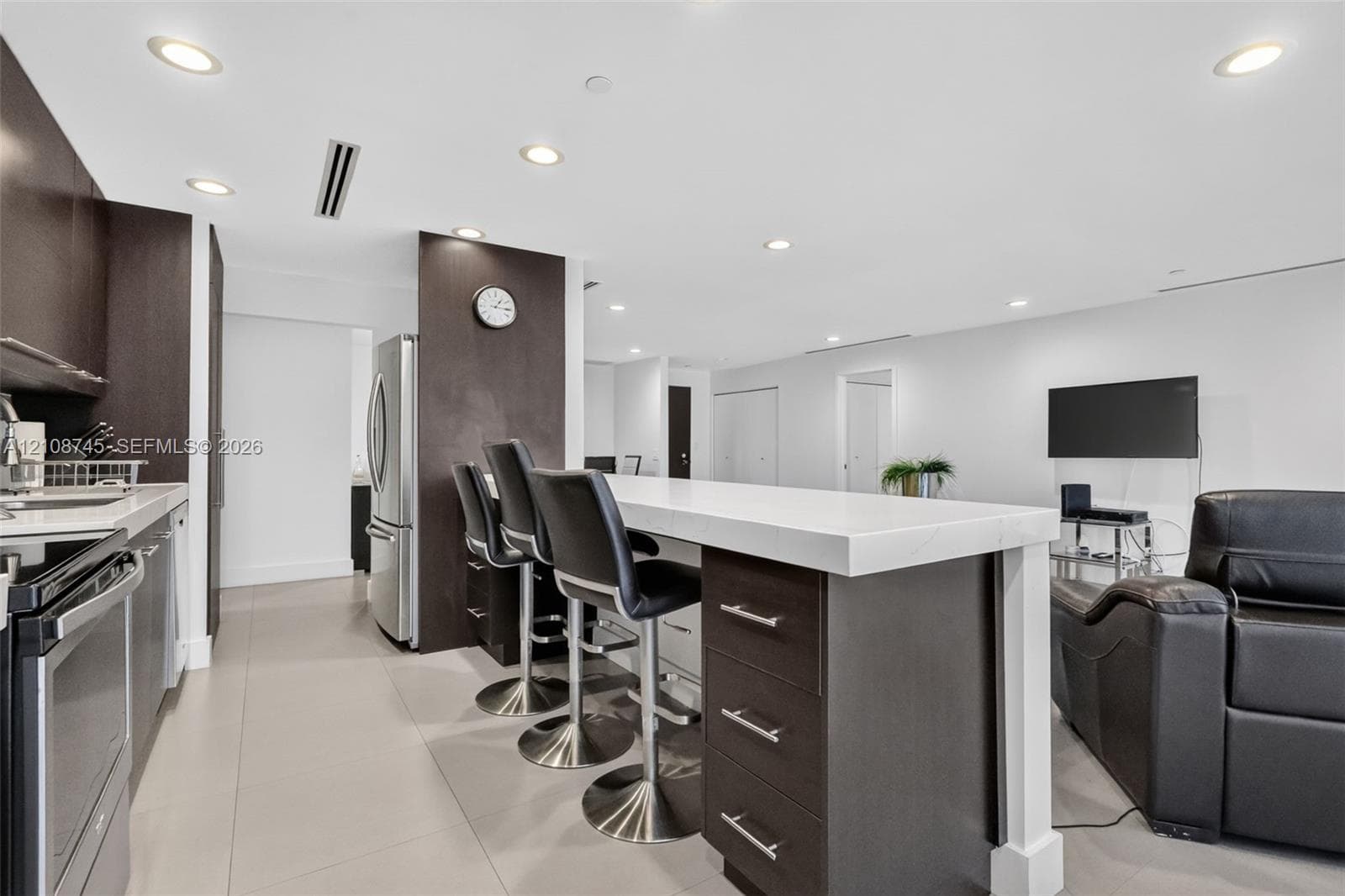 Kitchen featuring dark-finish cabinetry, an extended island with thick-edge countertops, stainless steel appliances, and large-format tile flooring