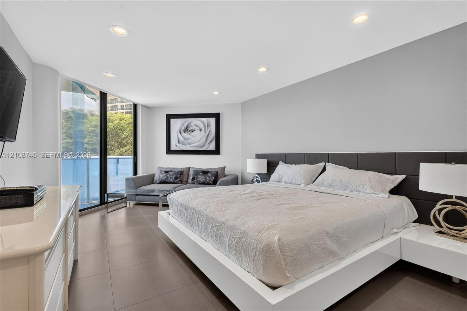 Floor-to-ceiling windows, large-format tile flooring, recessed ceiling lighting, and a dark, paneled built-in headboard