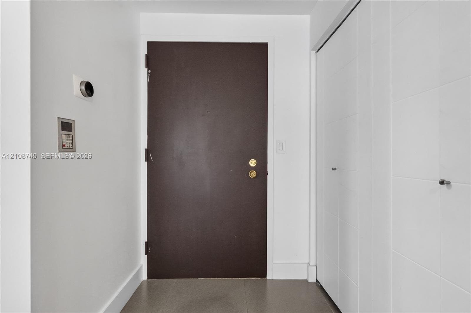 Entryway featuring a dark solid-core door, built-in floor-to-ceiling cabinetry with white panel doors, wall-mounted smart thermostat, and integrated security intercom panel
