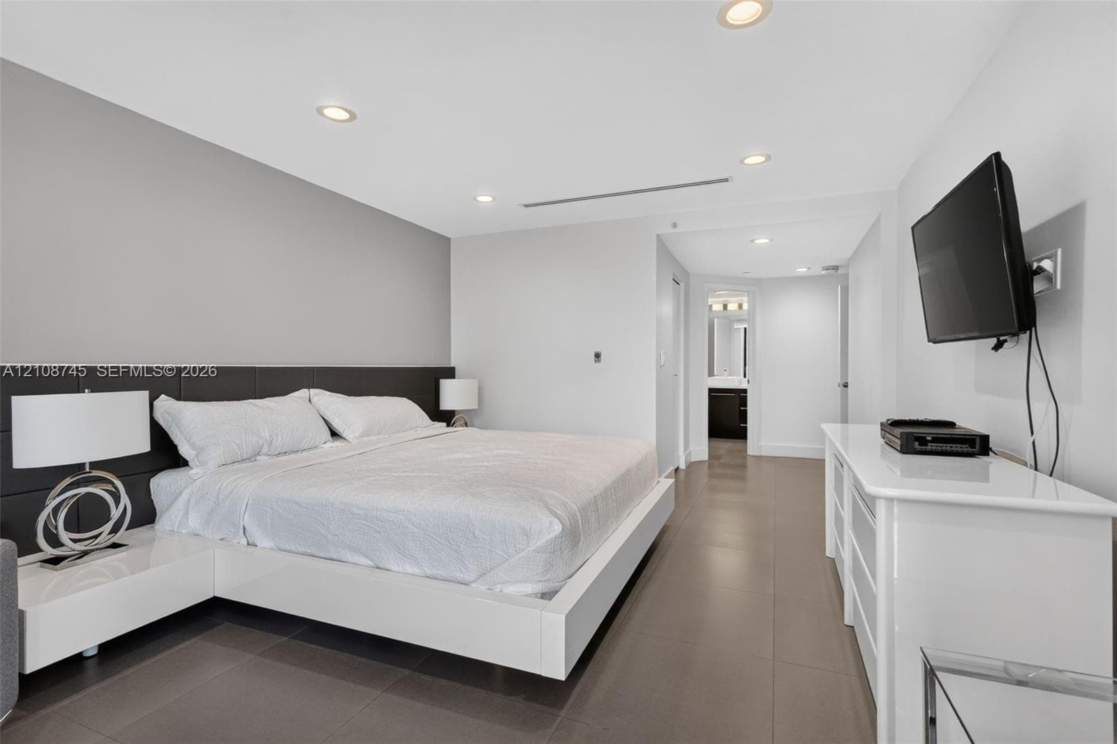 Neutral-toned room featuring large-format tile flooring, recessed ceiling lighting, and a dark integrated headboard panel