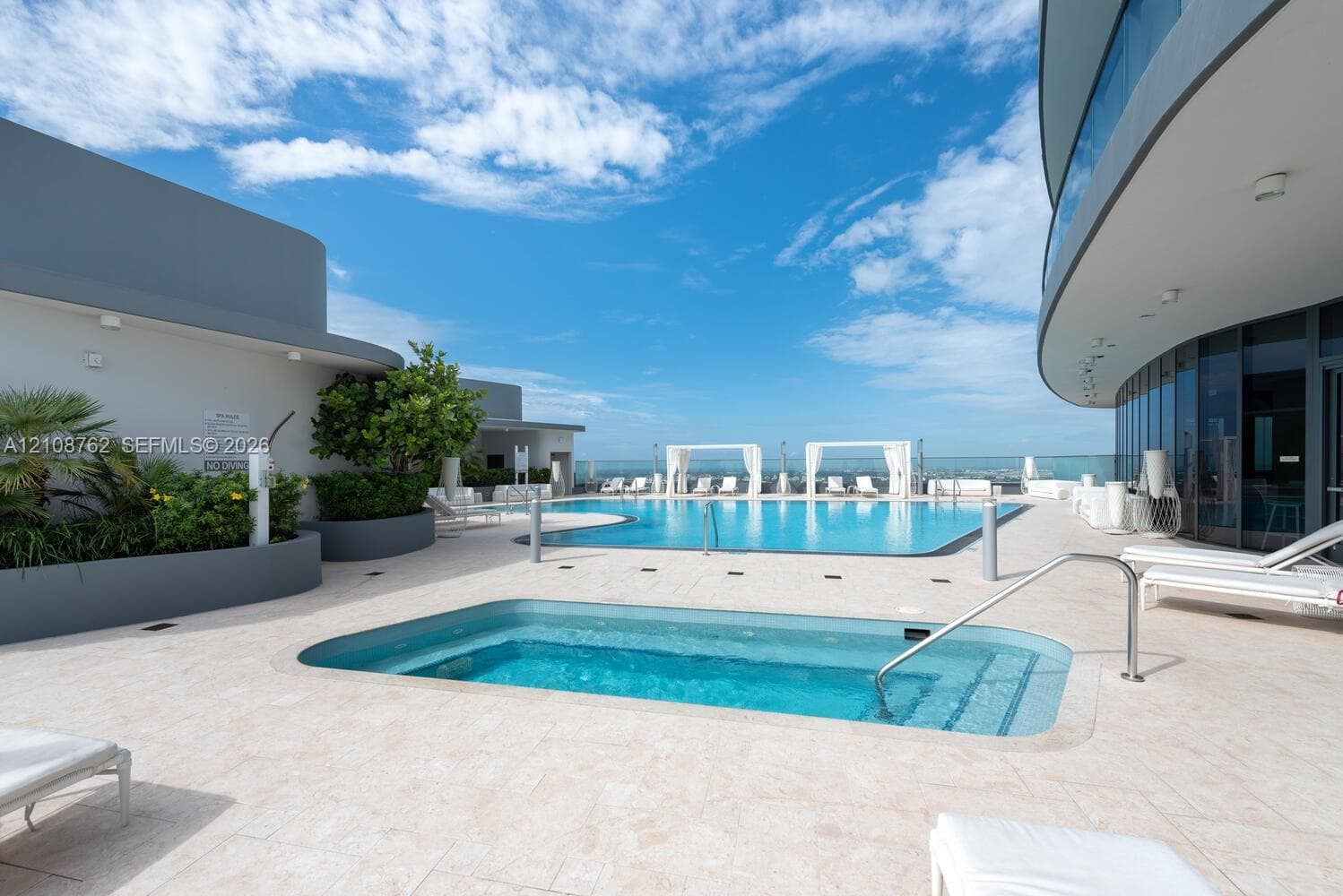 Rooftop terrace featuring an expansive swimming pool, integrated spa, stone-tile decking, and perimeter glass railing