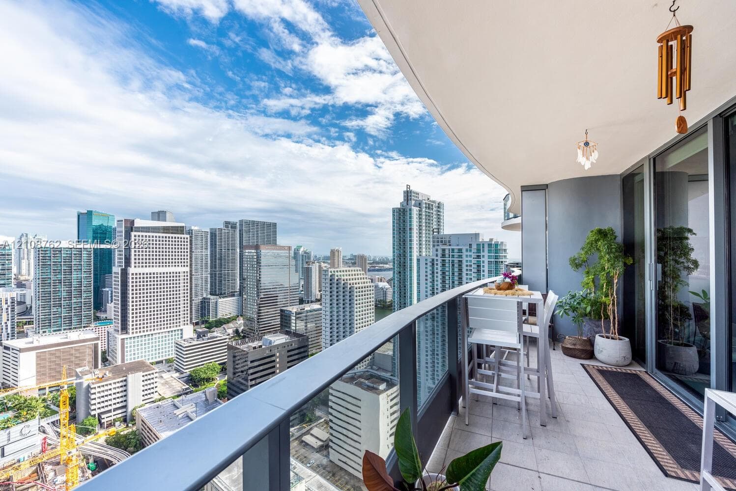 Covered private balcony featuring a glass-panel railing, light-tone tile flooring, and integrated wall-mounted lighting