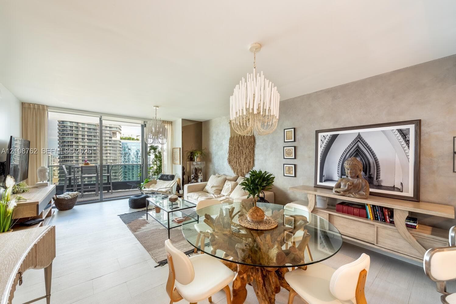 Open-concept interior featuring light-toned flooring, textured accent wall, dual statement chandeliers, and sliding glass doors with balcony access