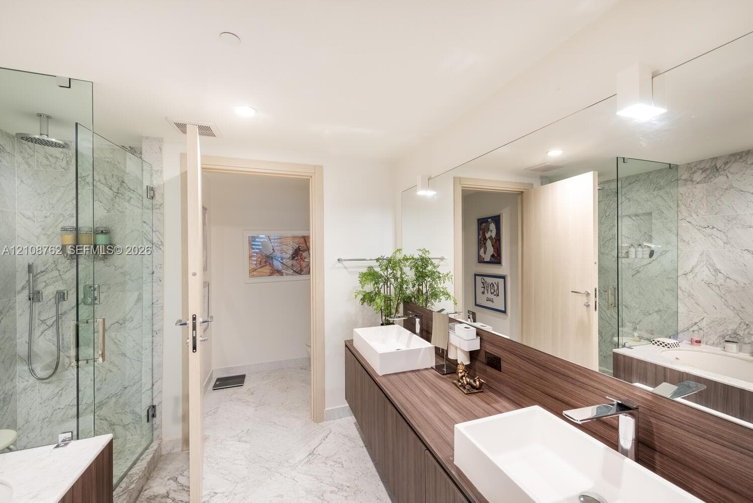 Walk-in shower with stone-tile surround, dual vessel sinks, wood-finish floating vanity, full-width wall mirror, and stone flooring