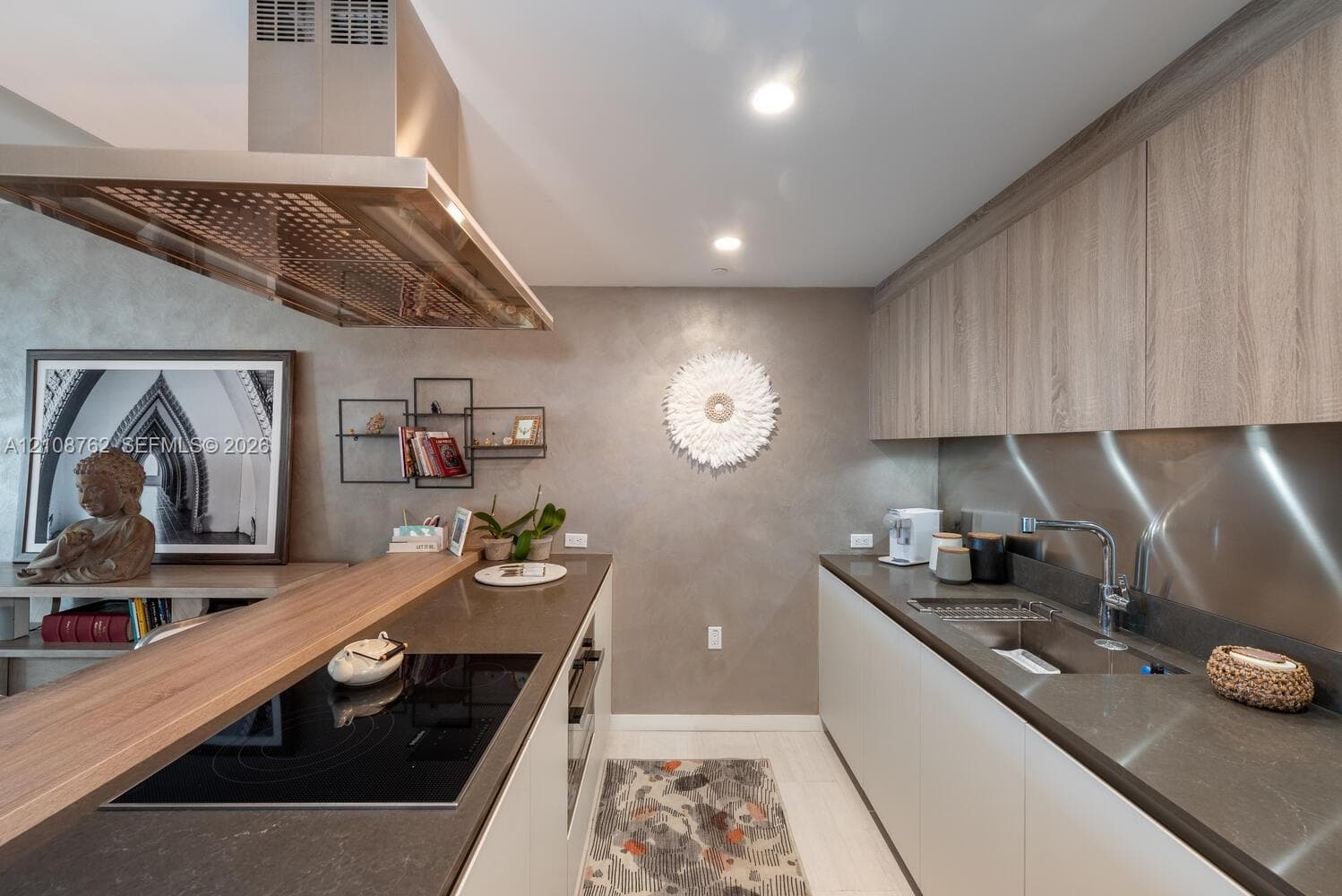 Contemporary kitchen featuring wood-grain cabinetry, sleek solid-surface countertops, a stainless steel backsplash, an integrated induction cooktop, and a stainless steel range hood