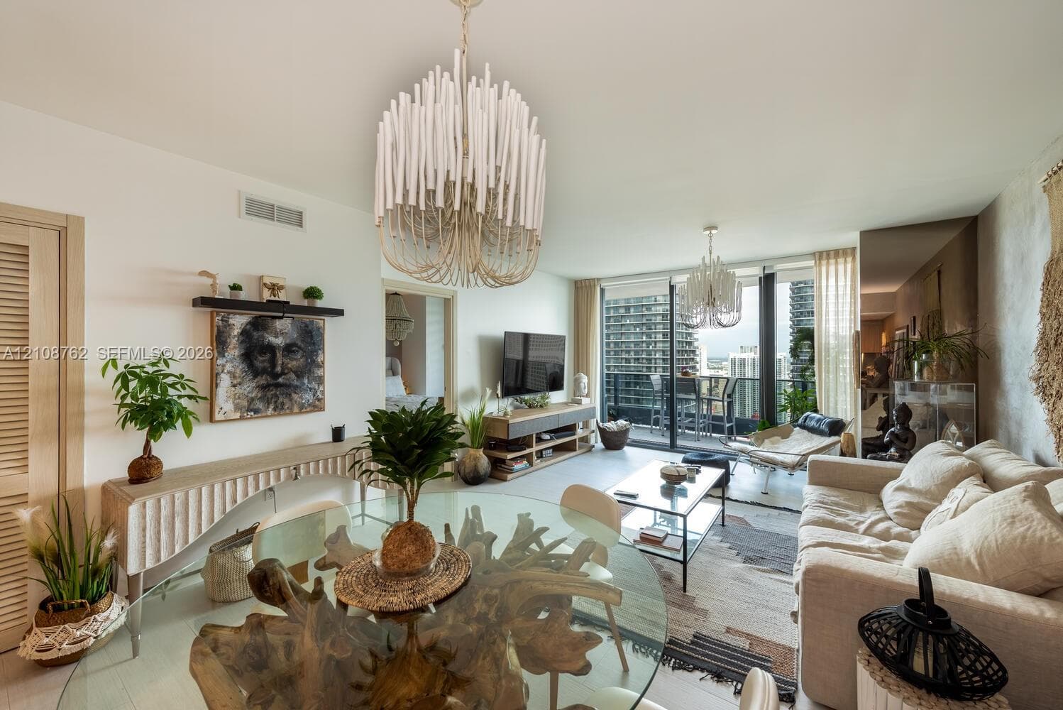 Open-concept living space featuring floor-to-ceiling glass doors, built-in mirrored wall panels, dual tiered-spindle chandeliers, and a private balcony