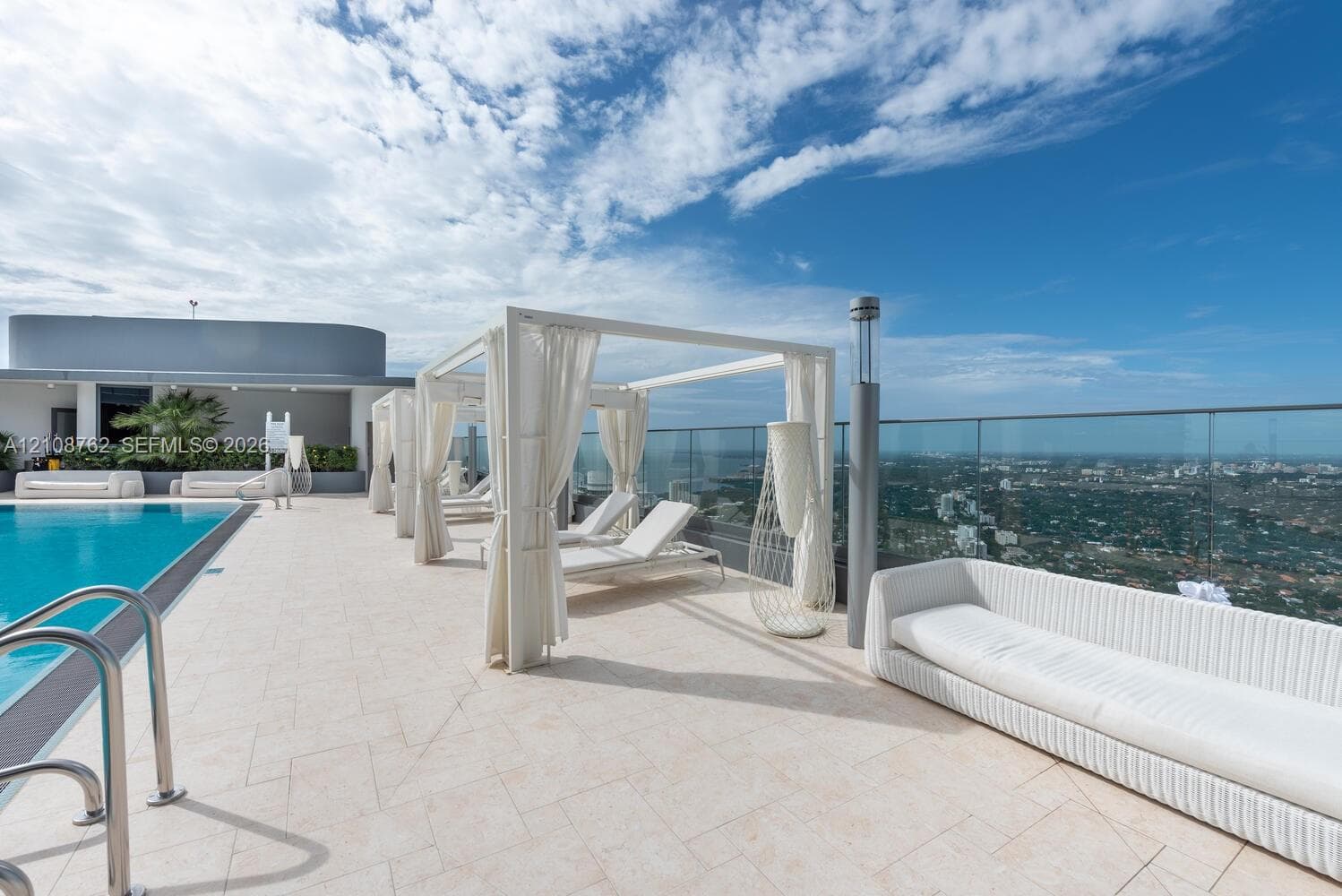 Rooftop pool deck featuring a tiled terrace, perimeter glass railing, built-in metal pool ladder, and structured cabanas