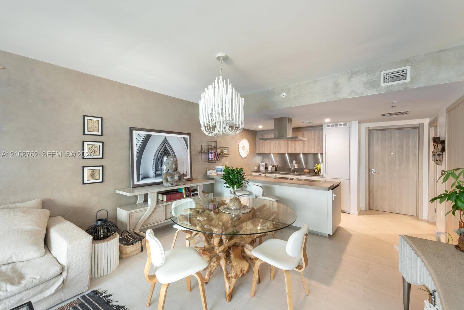 Open-concept space featuring light wood-finish flooring, a contemporary chandelier, textured wall finishes, and a kitchen with stainless steel backsplash and built-in cabinetry