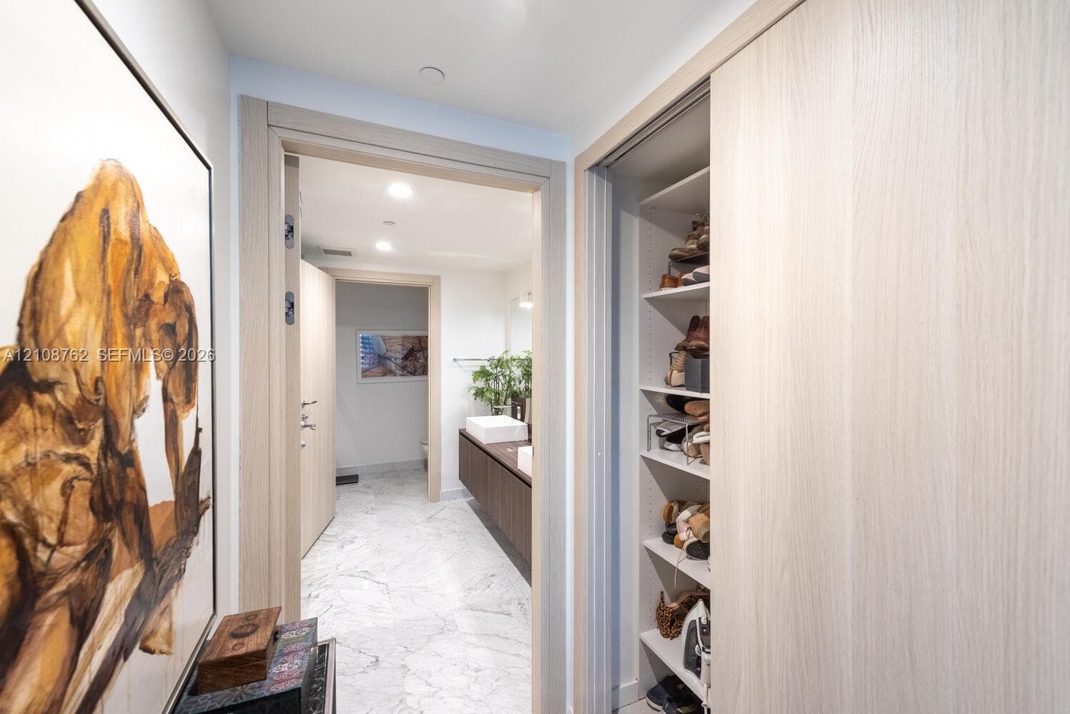 Built-in closet with light-toned cabinetry and shelving, polished stone flooring, and recessed ceiling lighting