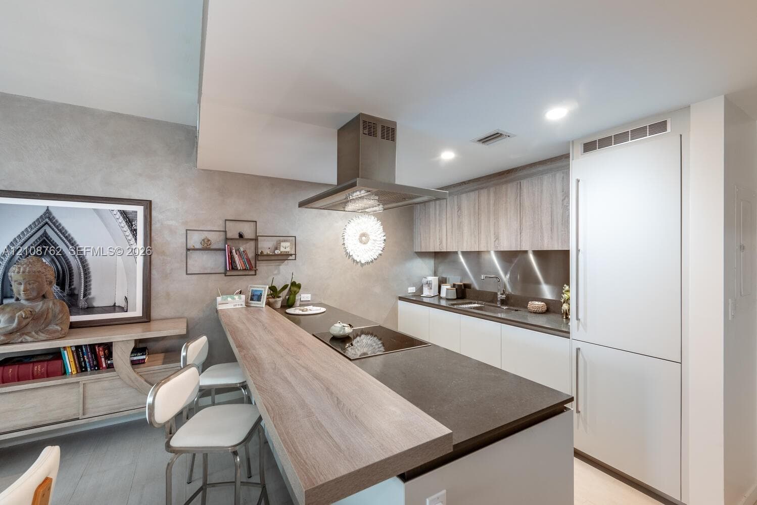 Kitchen featuring a flat-panel cabinetry, a wood-finish breakfast bar, a stainless steel range hood, stone-finish countertops, and an integrated refrigerator