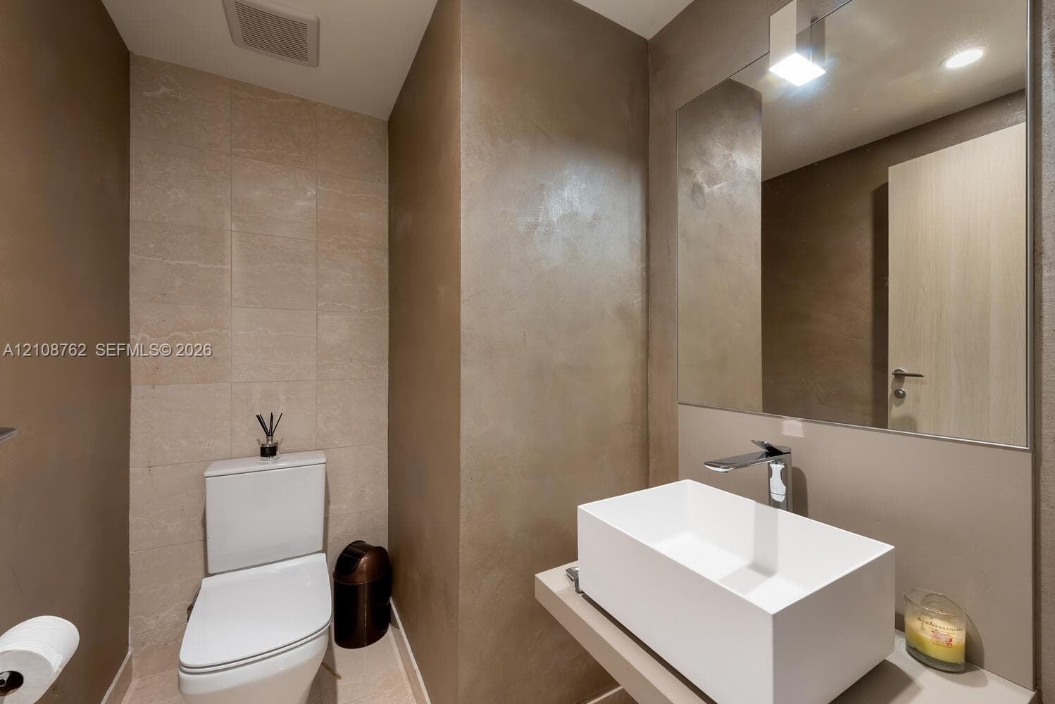 Modern wall-mounted vanity featuring a rectangular vessel sink and polished chrome faucet, paired with a large frameless mirror and textured wall surfacing