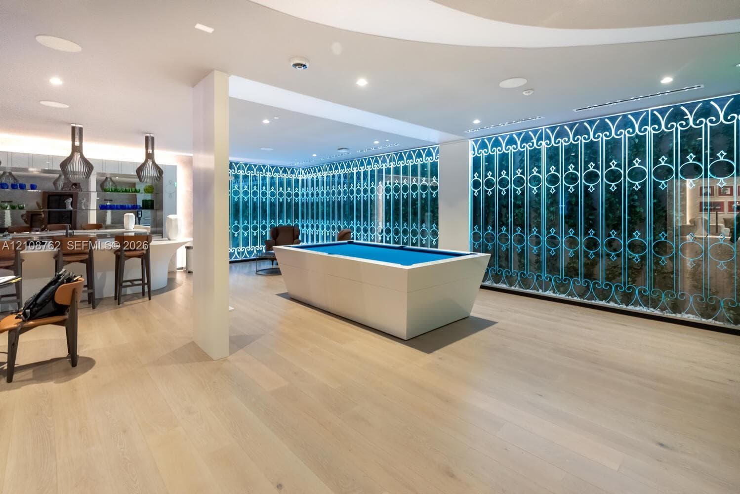 Open-concept interior featuring light wood-finish flooring, recessed ceiling lighting, a curved built-in bar, and floor-to-ceiling glass wall panels with ornamental decorative grillwork