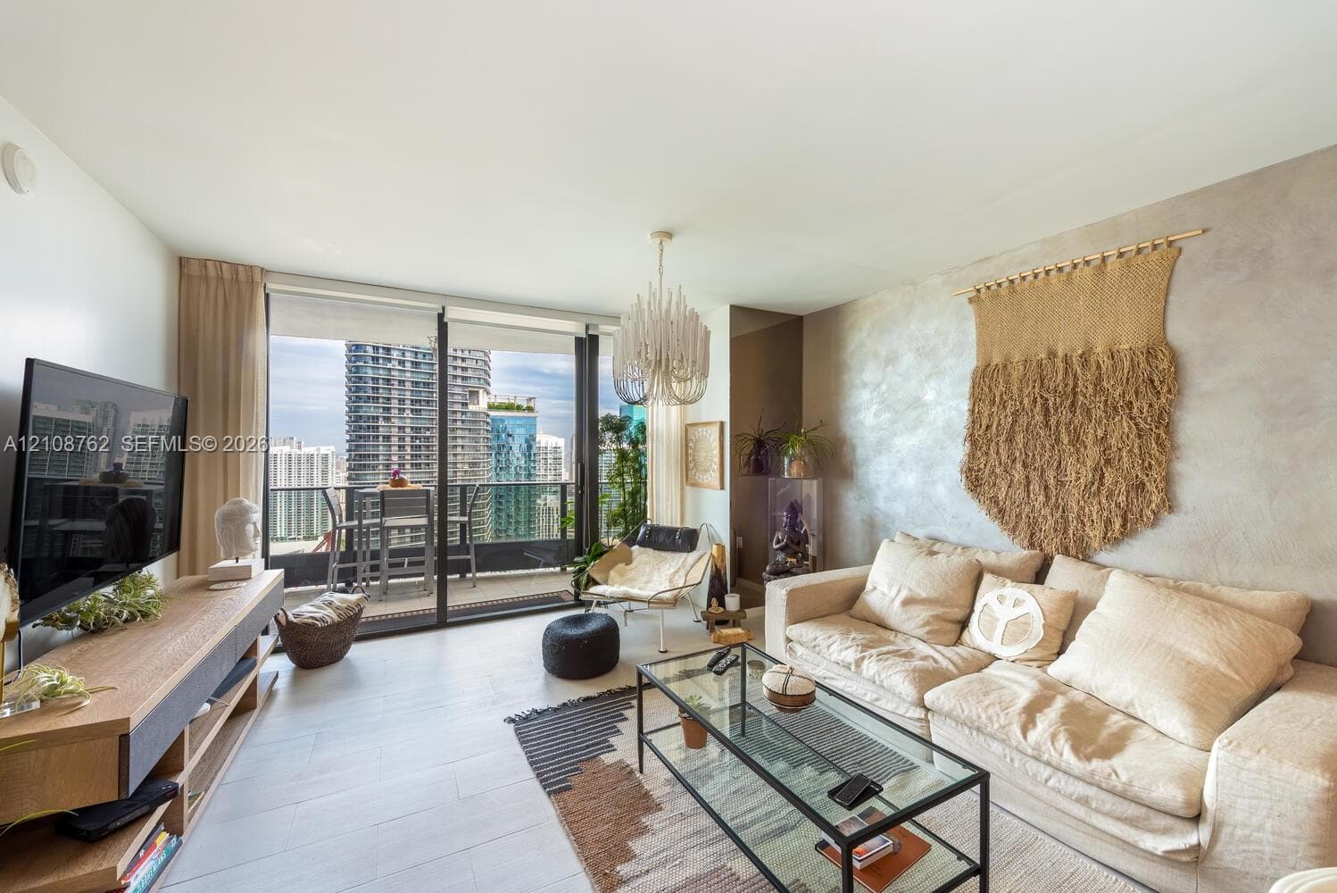 Living area featuring large-format tile flooring, floor-to-ceiling sliding glass doors, a private balcony, a decorative chandelier, and a textured feature wall