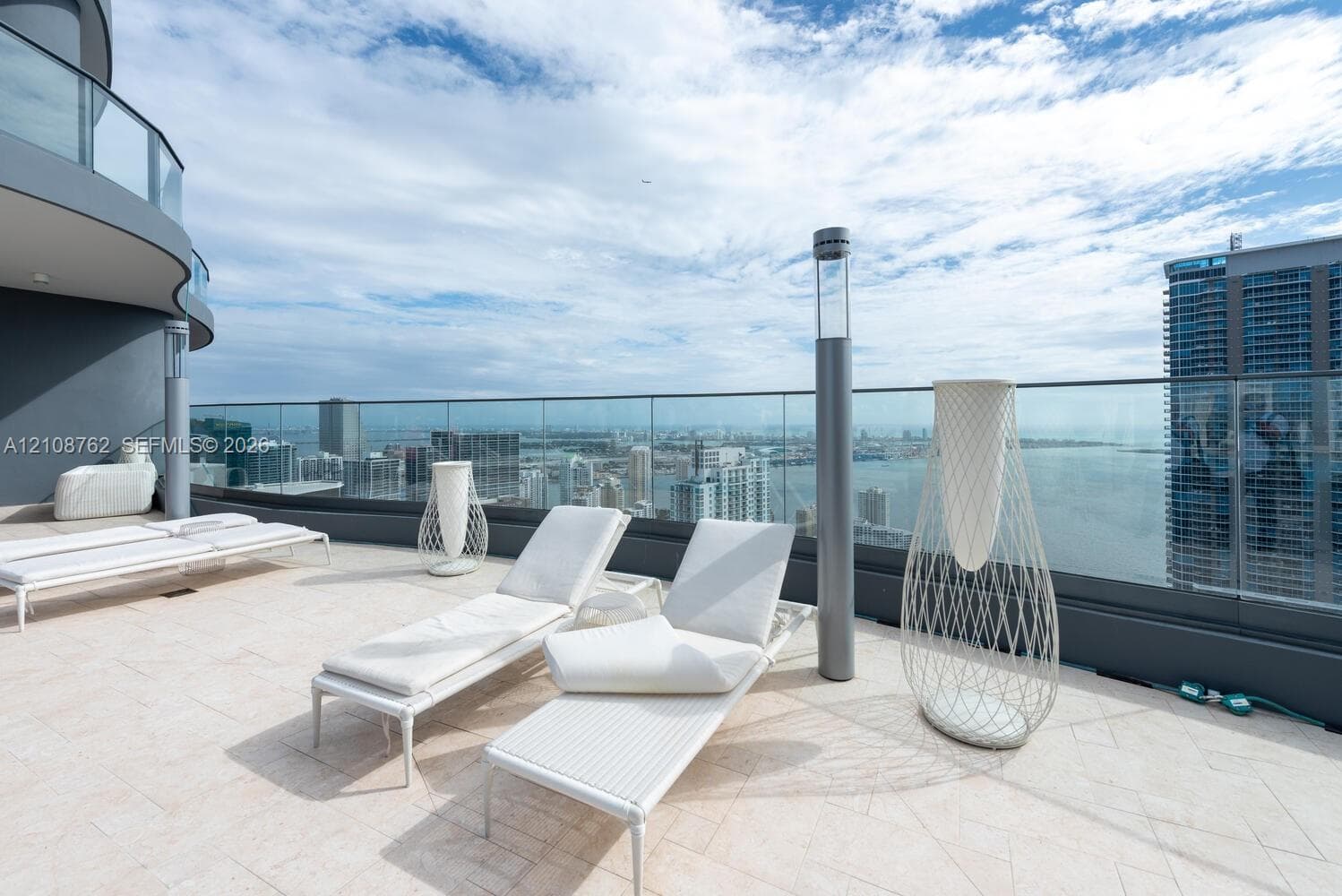Expansive terrace featuring light-toned stone tile flooring, a frameless glass balustrade, and integrated cylindrical light fixtures