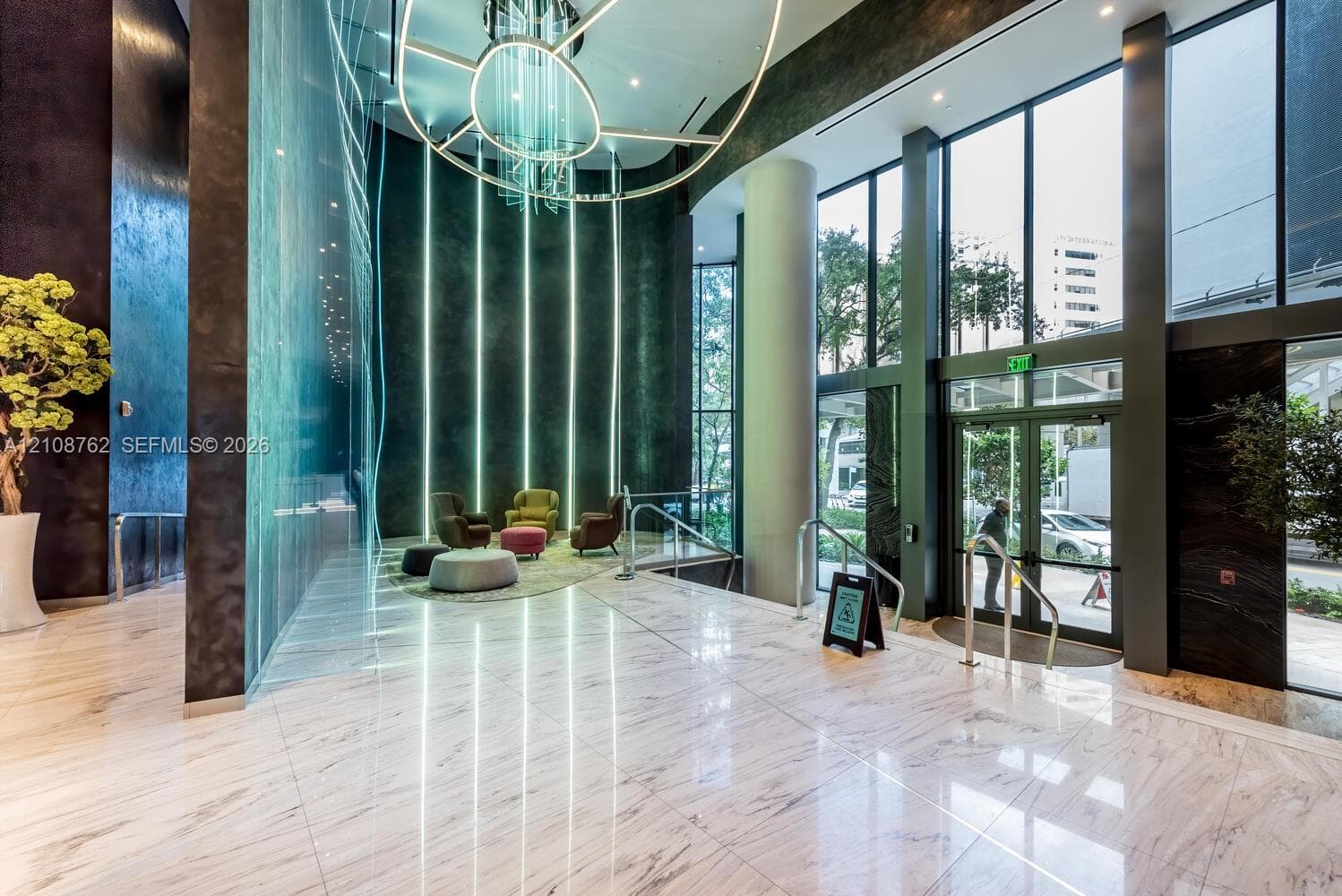 Grand lobby featuring floor-to-ceiling glass windows, stone-finish flooring, a multi-story feature wall with integrated vertical lighting, and a large-scale suspended circular chandelier