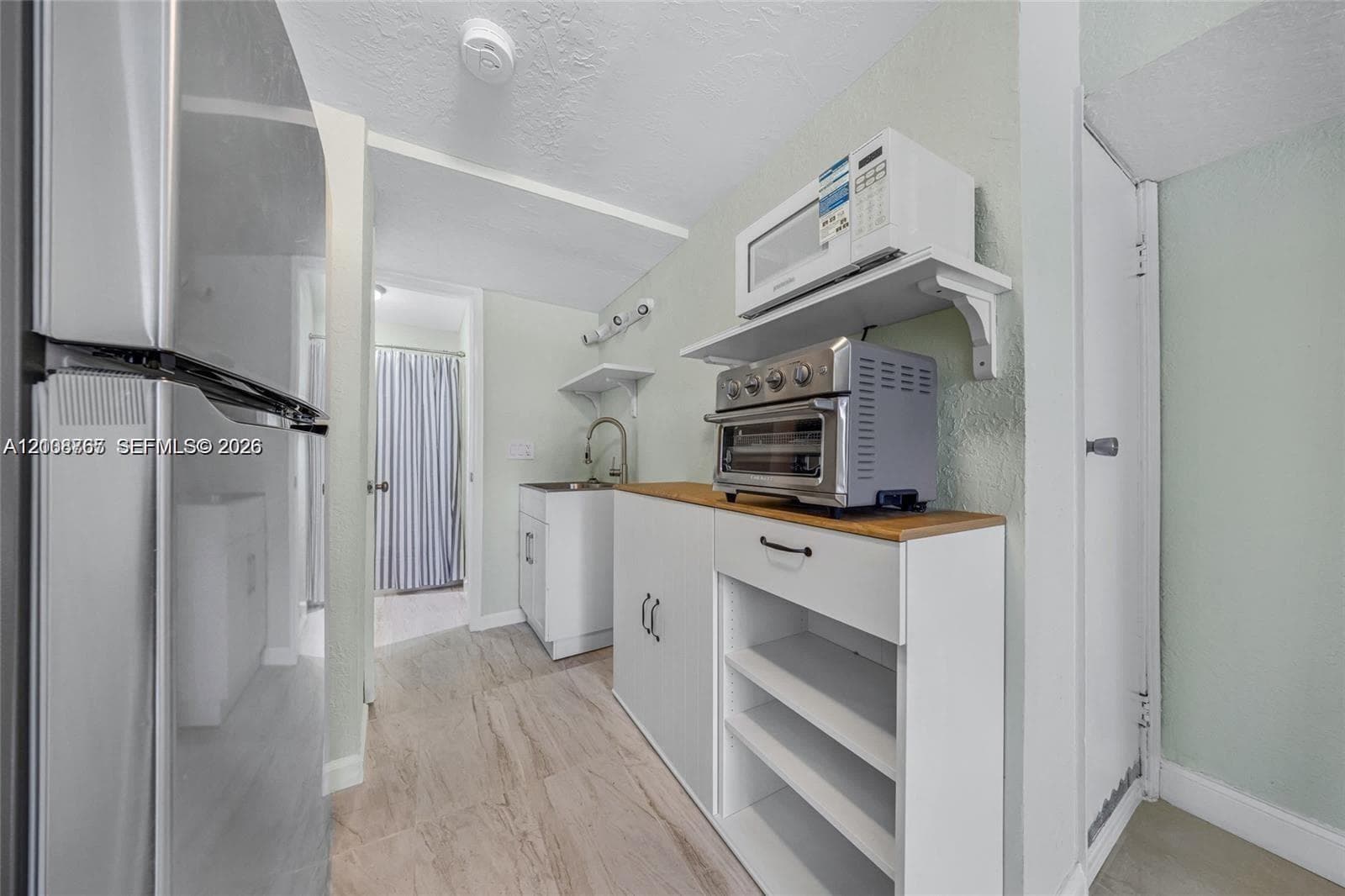 Kitchenette featuring white cabinetry, wood-surface countertop, stainless steel refrigerator, and integrated shelving