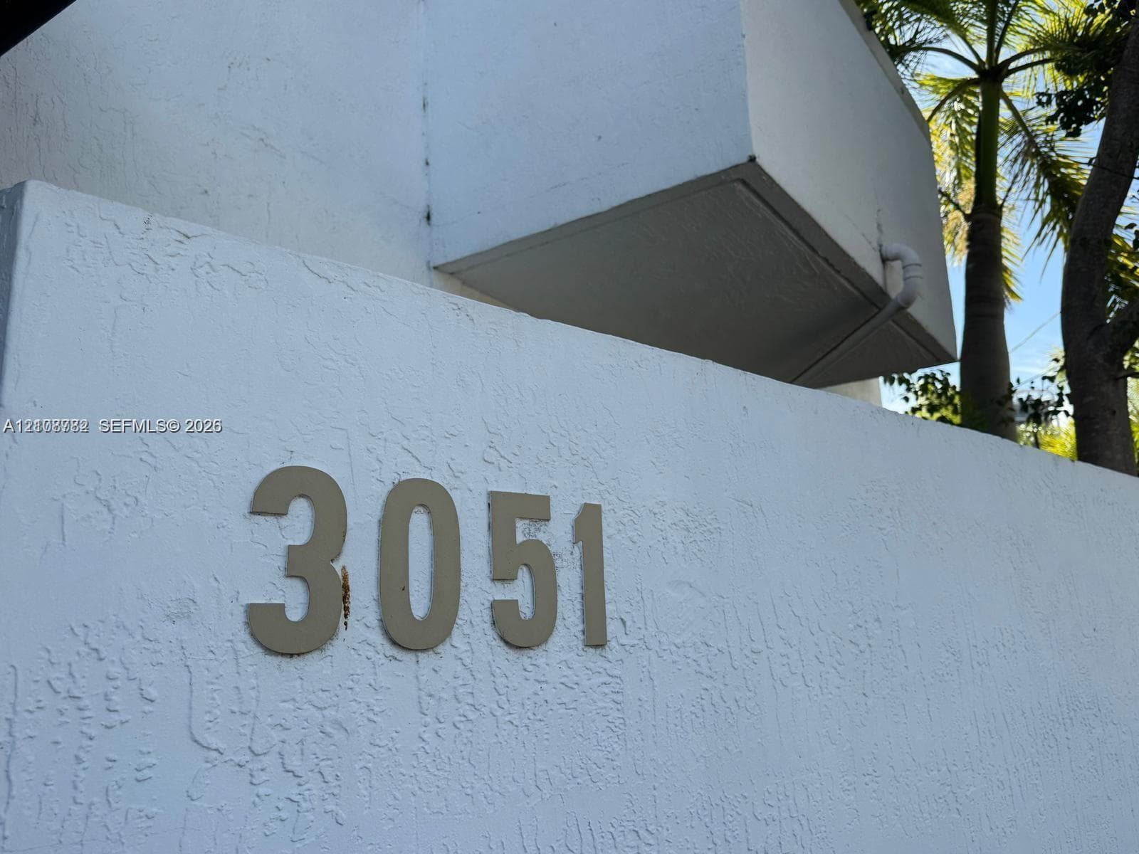 Stucco exterior wall featuring three-dimensional address numerals and mature palm tree landscaping