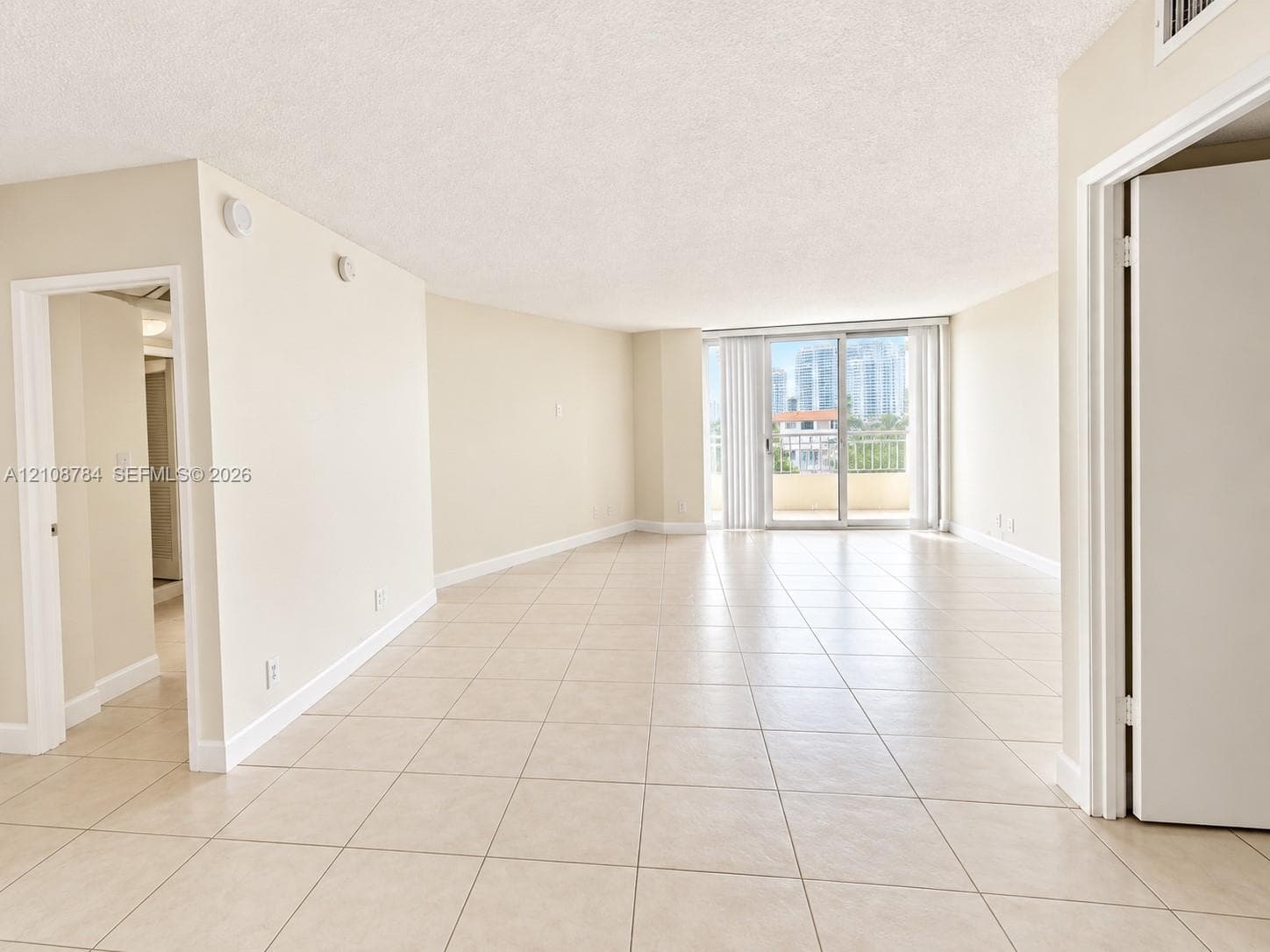 Open-concept interior featuring large-format tile flooring, textured ceilings, neutral paint palette, and sliding glass doors providing outdoor access