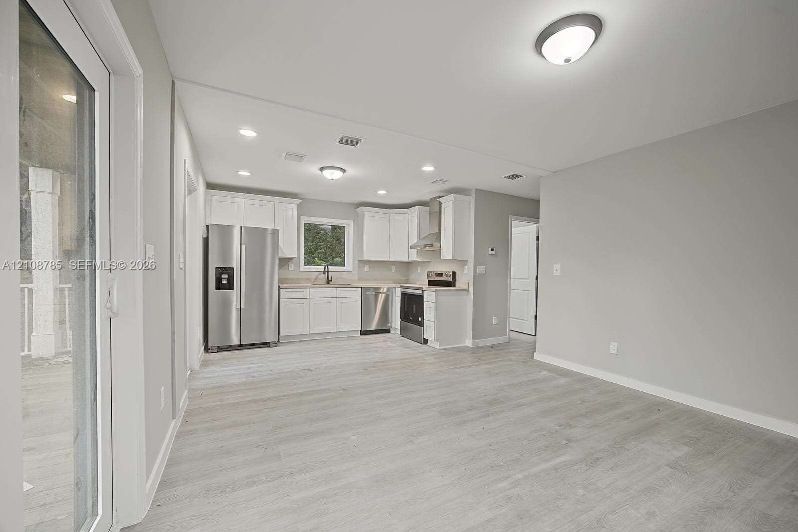 Kitchen featuring white cabinetry, stainless steel appliances, wood-finish flooring, recessed lighting, and a sliding glass door