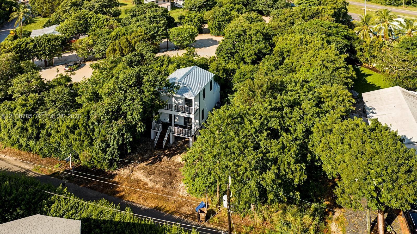 Two-story elevated structure featuring a metal roof, stacked exterior balconies, and a tree-lined lot