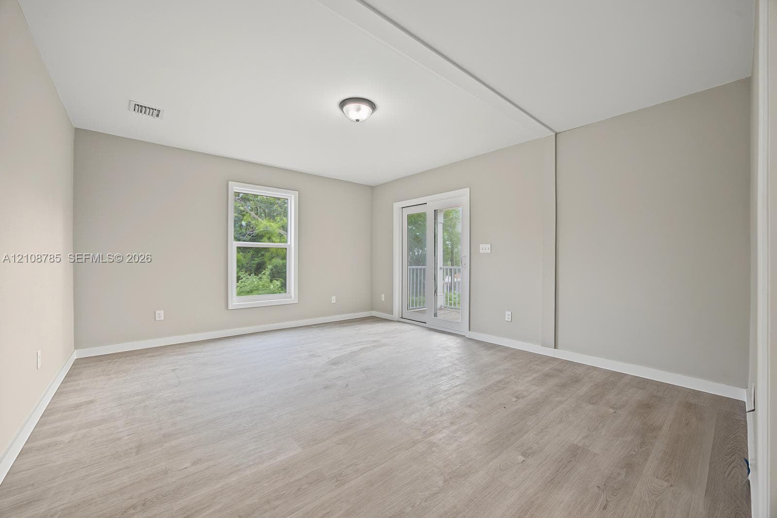 Neutral-toned interior featuring wood-finish flooring, a glass-pane sliding door with exterior access, a single window, and a flush-mount ceiling light fixture