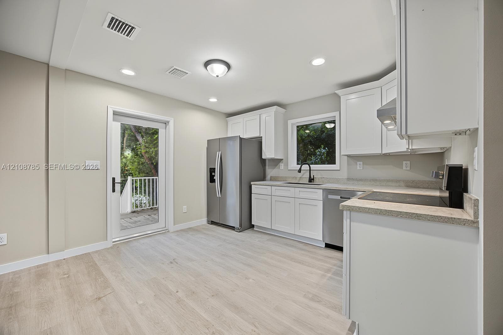 Kitchen featuring white cabinetry, stone-finish countertops, stainless steel appliances, a deep-basin sink with a matte black faucet, and wood-finish flooring