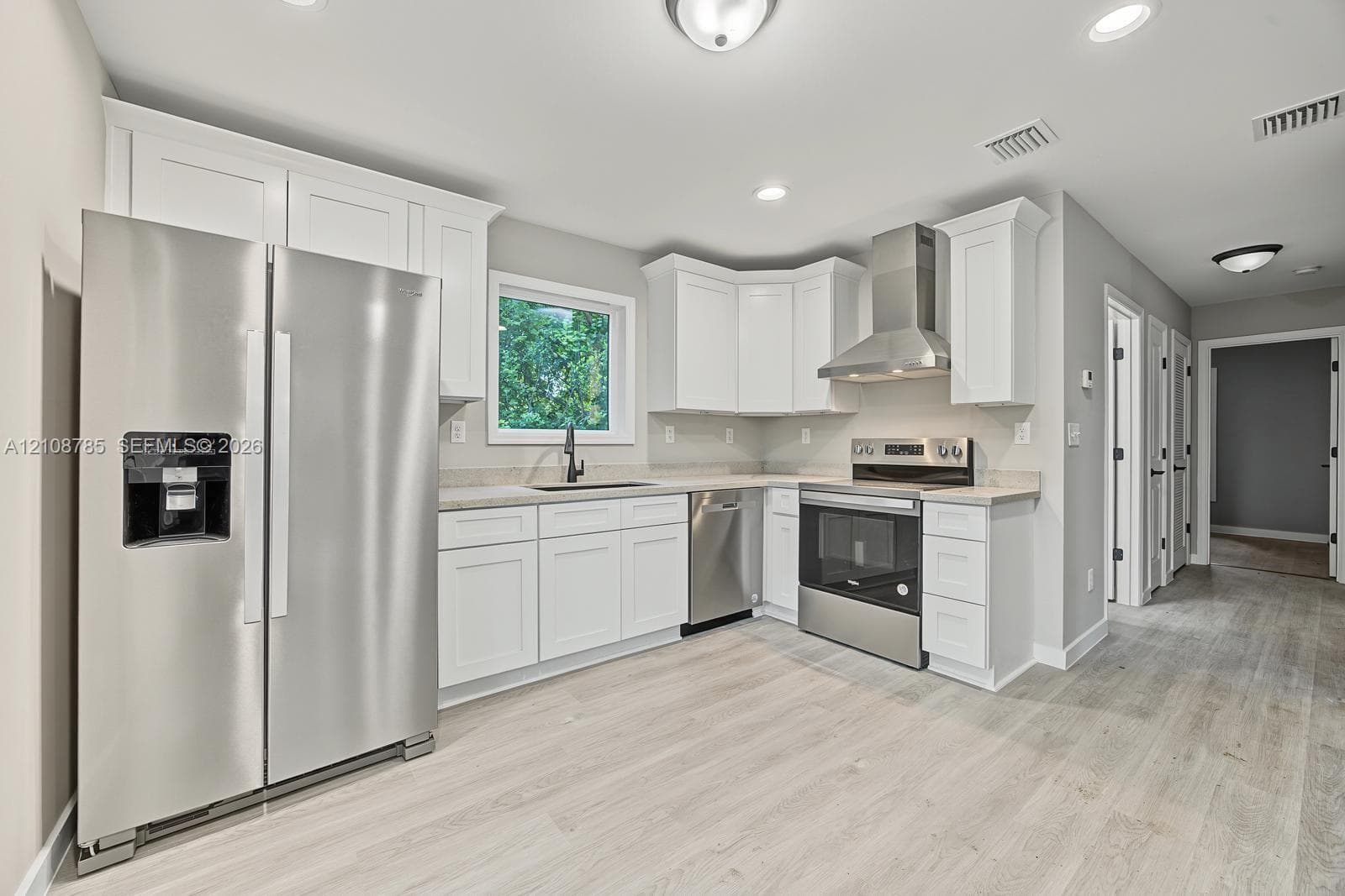 Kitchen featuring white shaker-style cabinetry, stainless steel appliances, a stainless steel range hood, stone-finish countertops, and wood-finish flooring