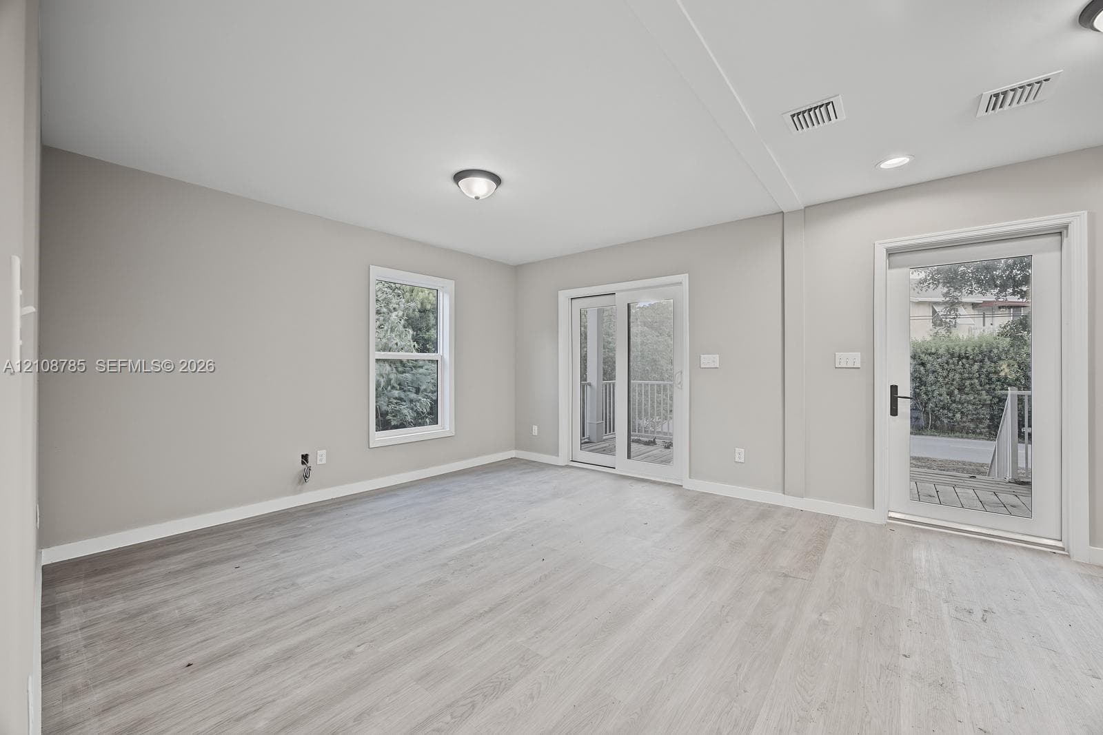 Neutral-toned interior space featuring wood-finish flooring, sliding glass patio doors, a separate exterior door with a glass pane, and recessed ceiling lighting
