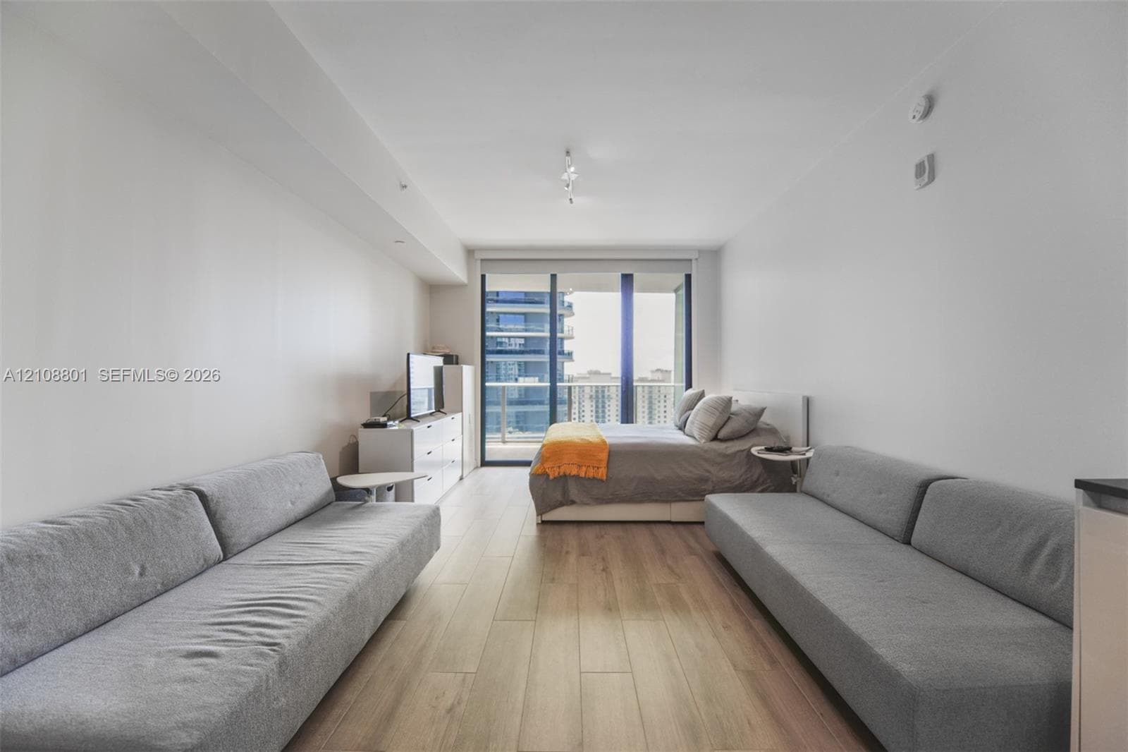 Open-concept room featuring wood-finish flooring, floor-to-ceiling glass sliding doors, and a private balcony