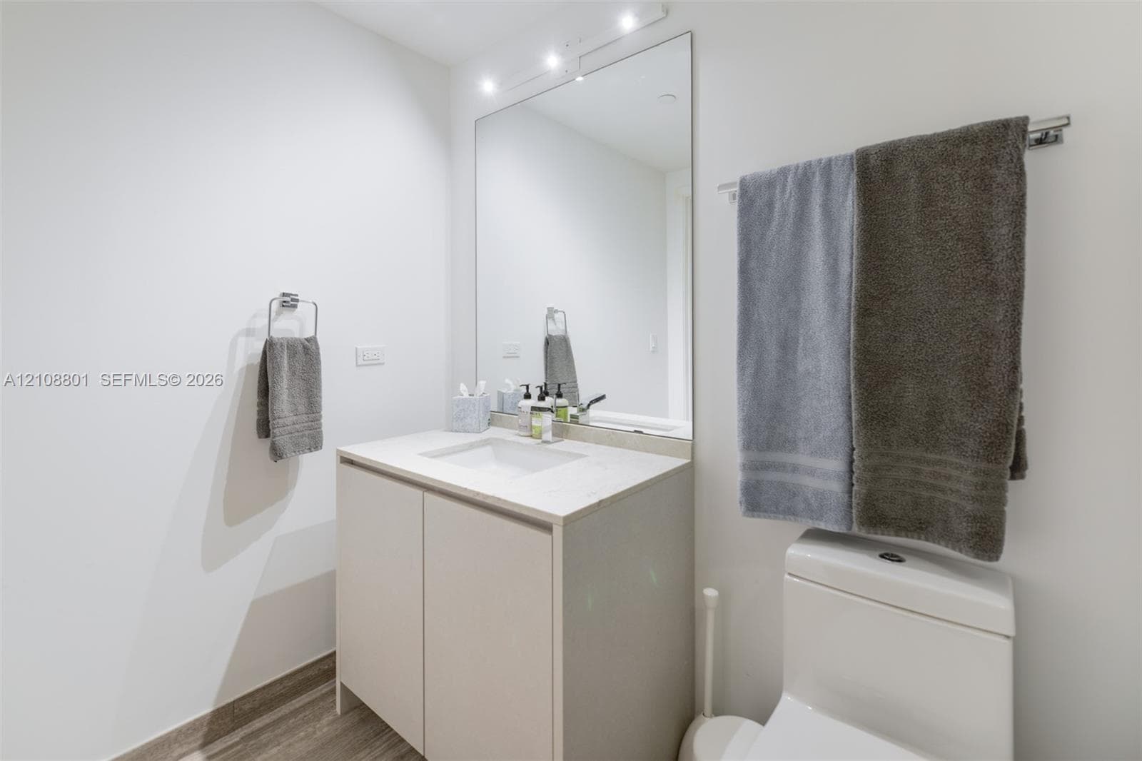 Vanity with a stone-surface countertop, integrated rectangular basin, full-height wall mirror, overhead lighting, and wood-finish flooring
